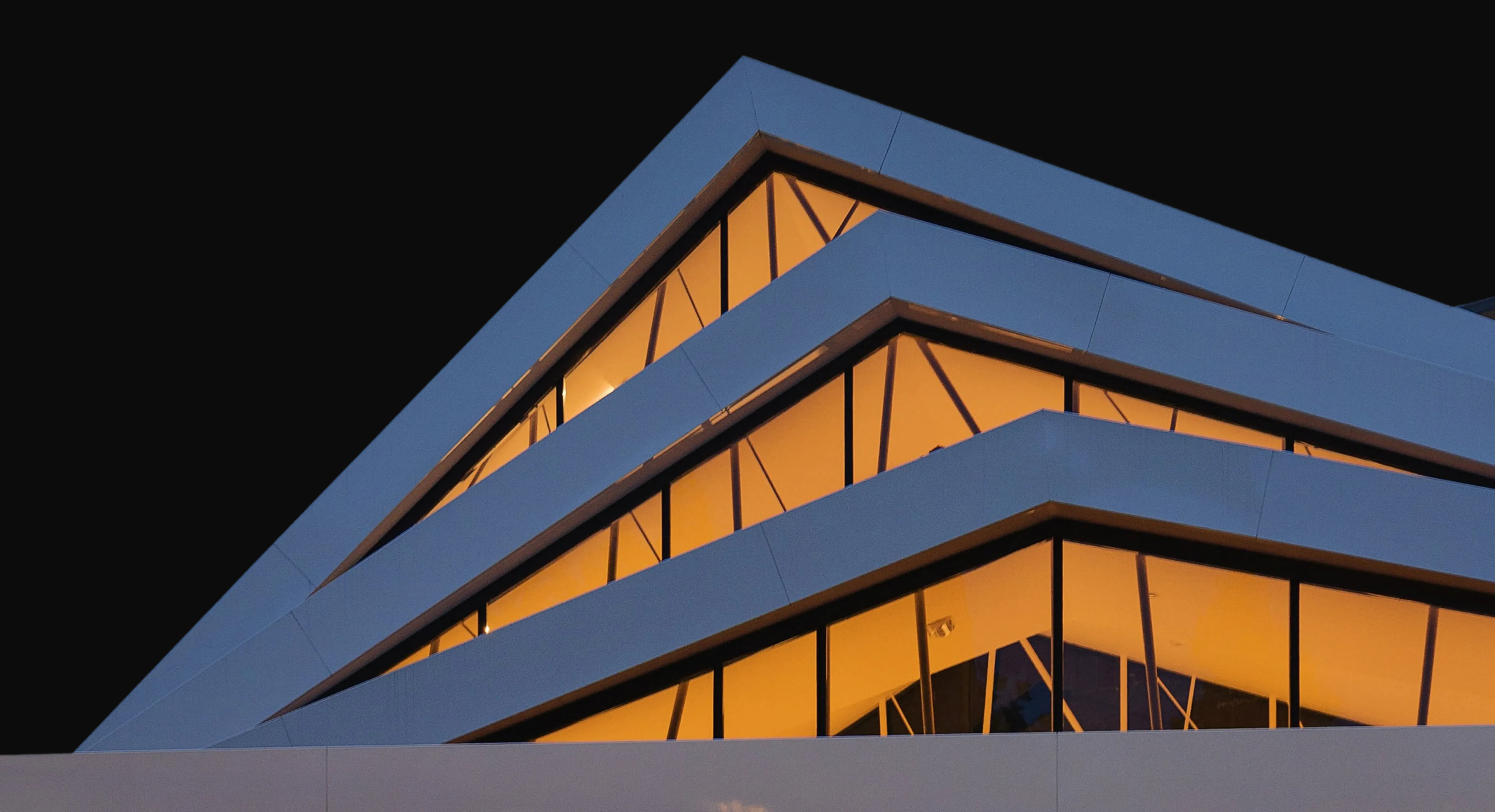 Angular modern building with tiered white rooflines and warm interior lighting against a dark night sky.