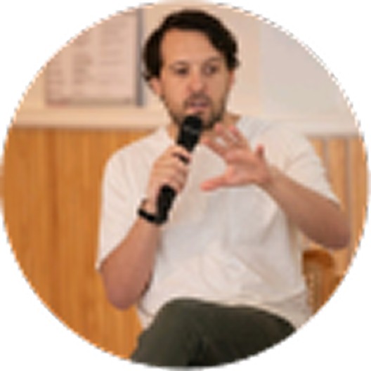 Editorial portrait of a young man with wavy hair in a knit sweater, looking over his shoulder in soft light.