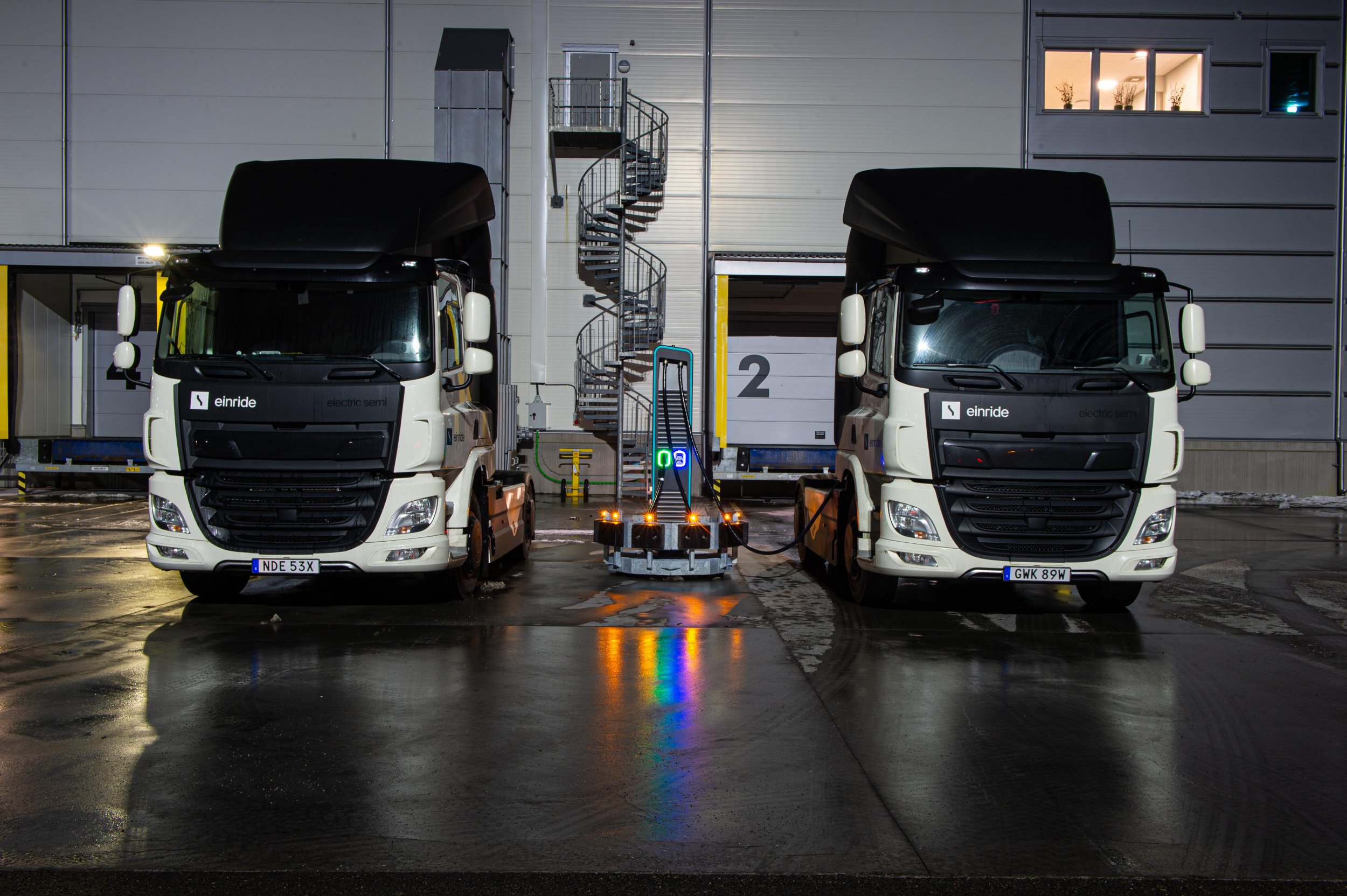 Two Einride electric vehicles parked at night in a warehouse, connected to a charging station.