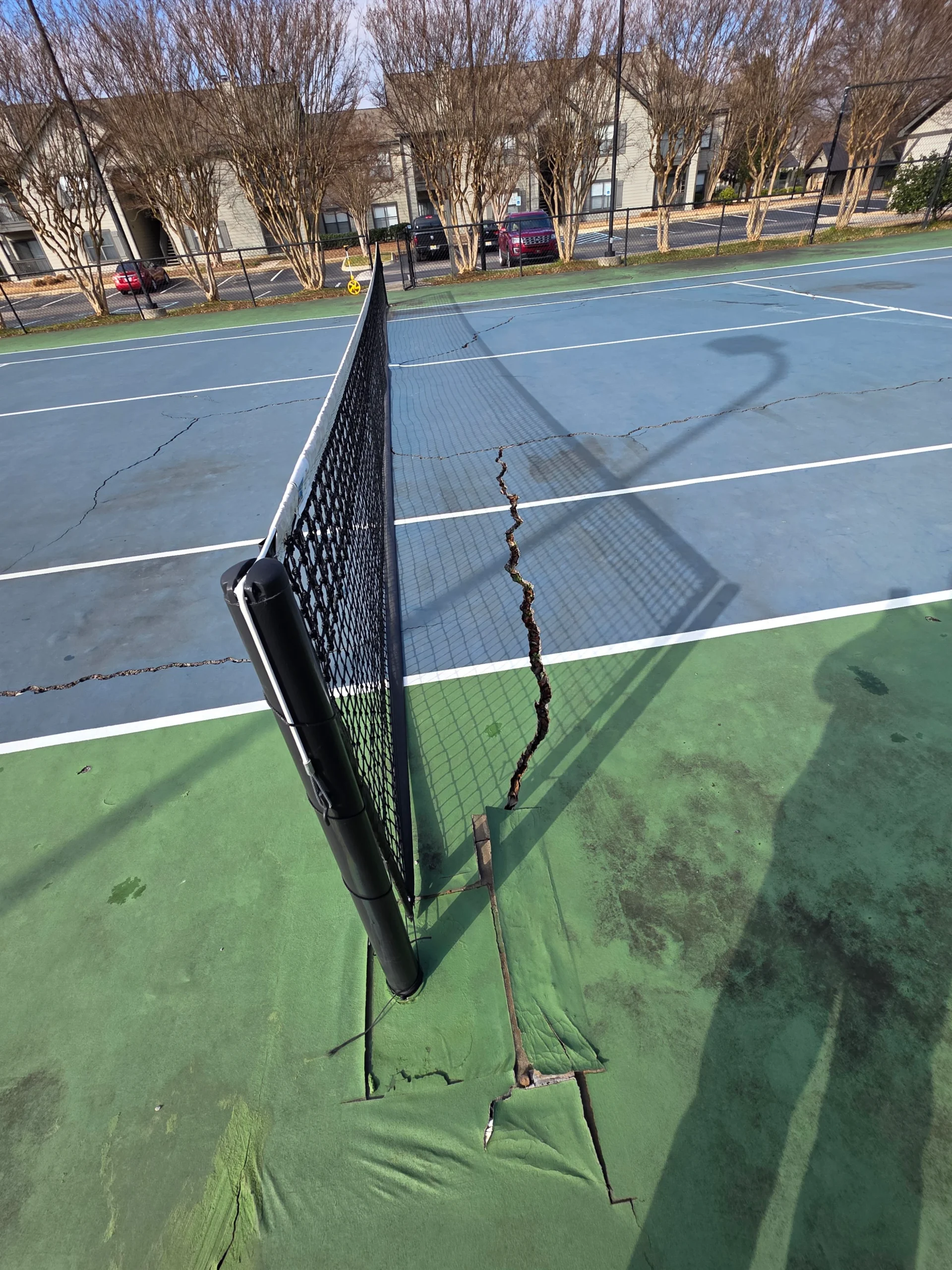 Cracked tennis court surface near the net post before resurfacing at Weston Ranch in Madison, AL