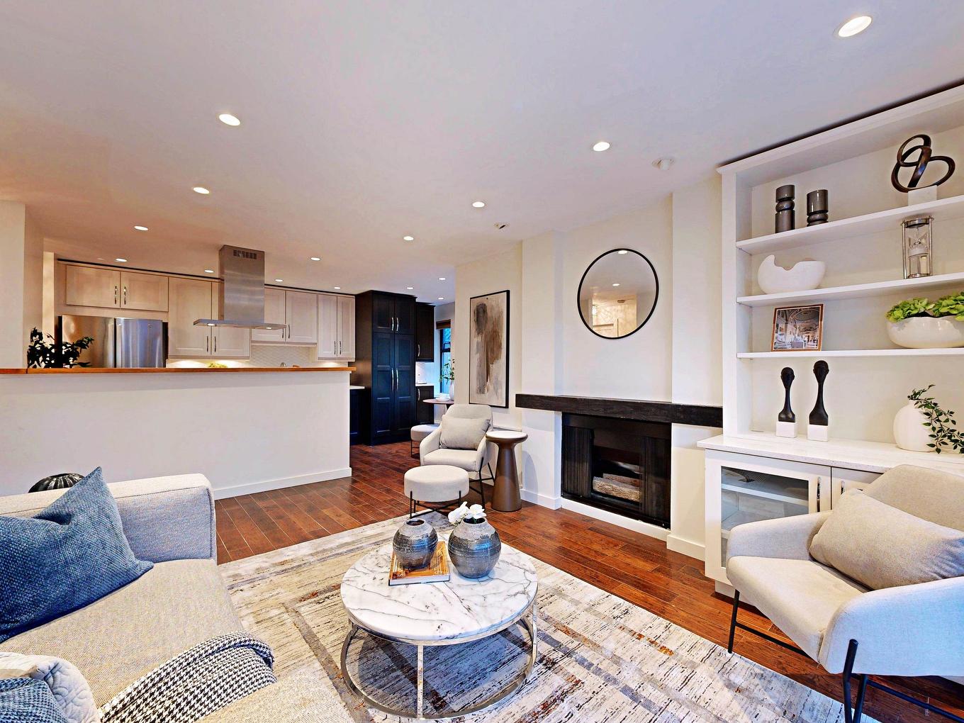 Modern living room with a cozy seating area, a coffee table, and a view of an open kitchen. Bright and inviting space.