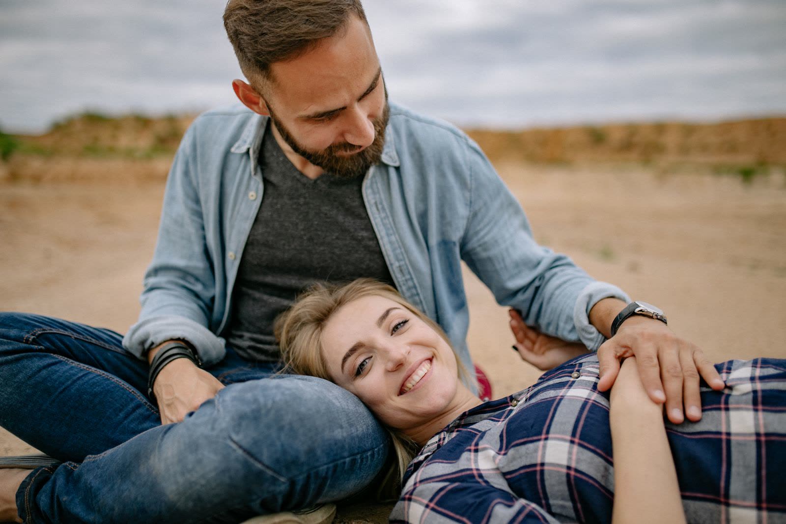 Smiling woman in a check shirt lying across the lap of a bearded man in a denim shirt