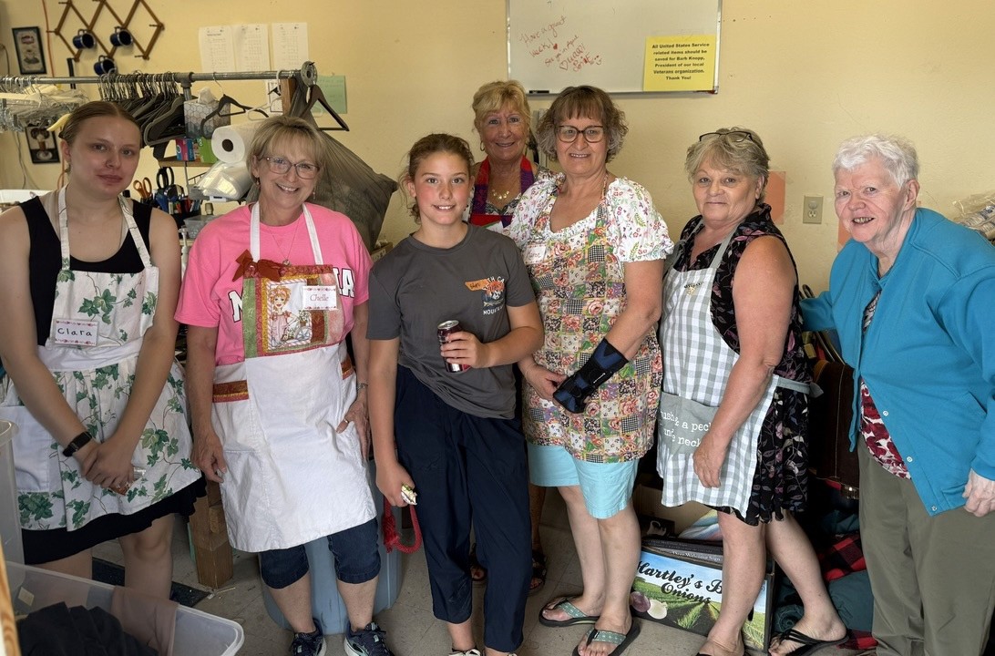 A girl standing with a group of women in aprons at a thrift store.