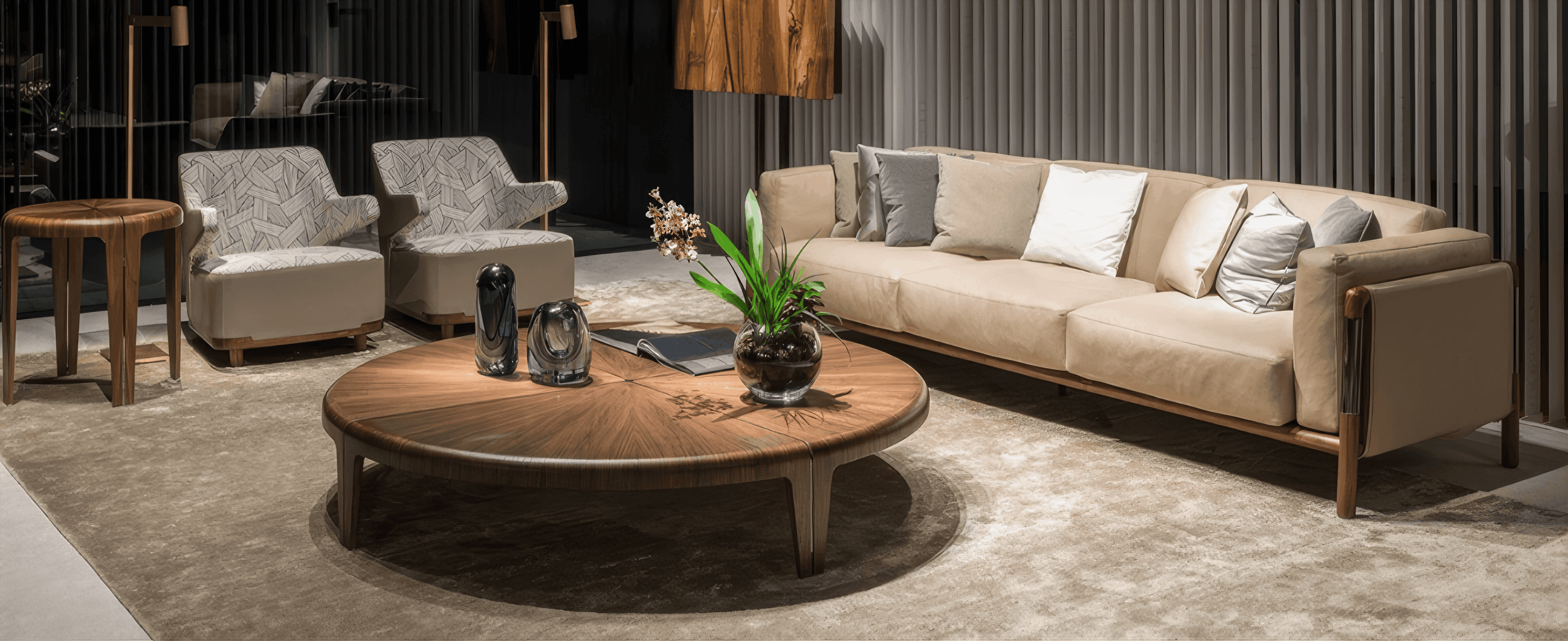 MW Interior - Beiges Designersofa mit Nussbaum-Couchtisch und gemustertem Sessel auf Hochflorteppich" Ein langes, sandfarbenes Sofa mit Holzrahmen in Nussbaum steht einem breiten, runden Couchtisch mit Furnier-Sonnenblume gegenüber. Daneben: ein Sessel mit geometrisch bedrucktem Bezug und ein kleiner Beistelltisch aus massivem Nussbaum. Der Hintergrund zeigt dunkel vertäfelte Wände mit Vorhangstreifen.