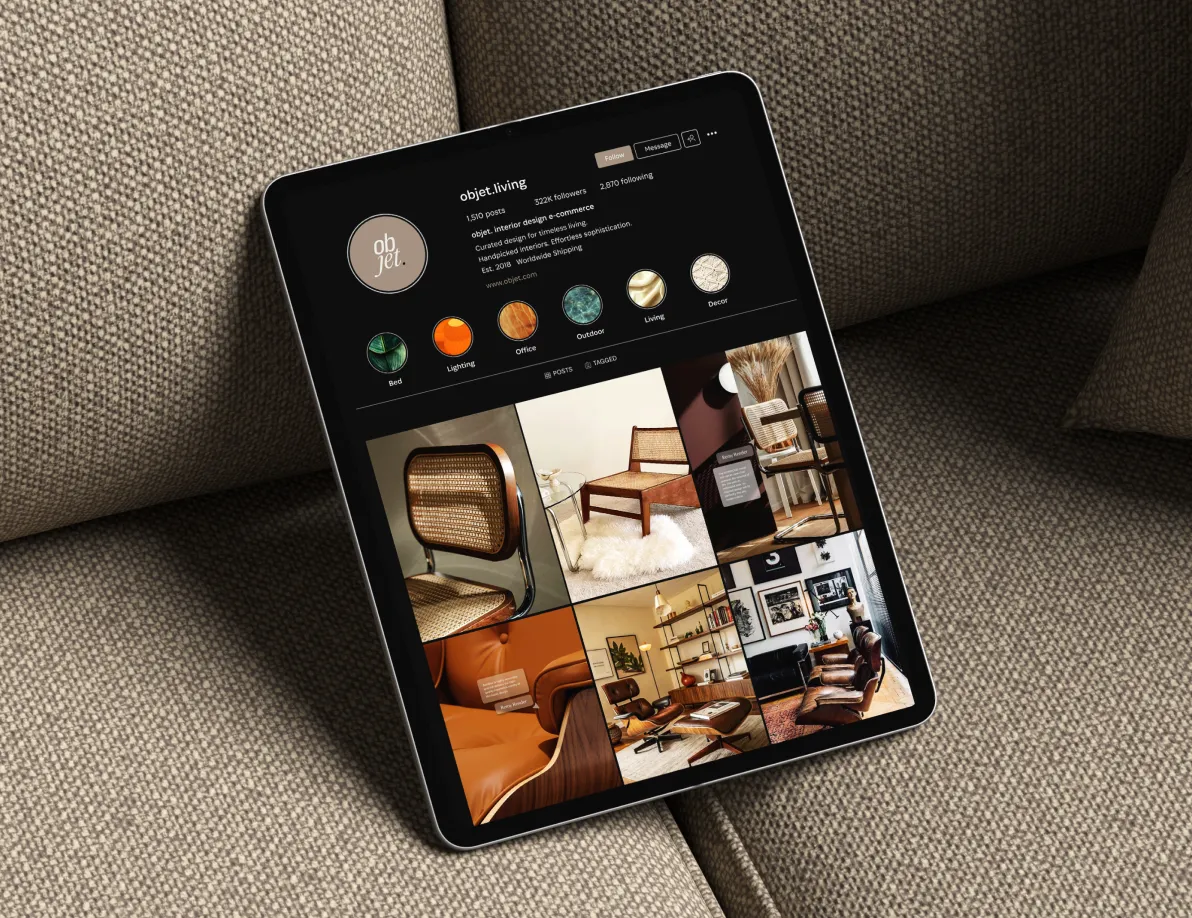 iPad leaning against a beige linen cushion, displaying the @objet.living Instagram profile with 322K followers — highlights organized by category including Bed, Lighting, Office, Outdoor, Living, and Decor — with a warm-toned feed grid of mid-century modern furniture and curated interior spaces