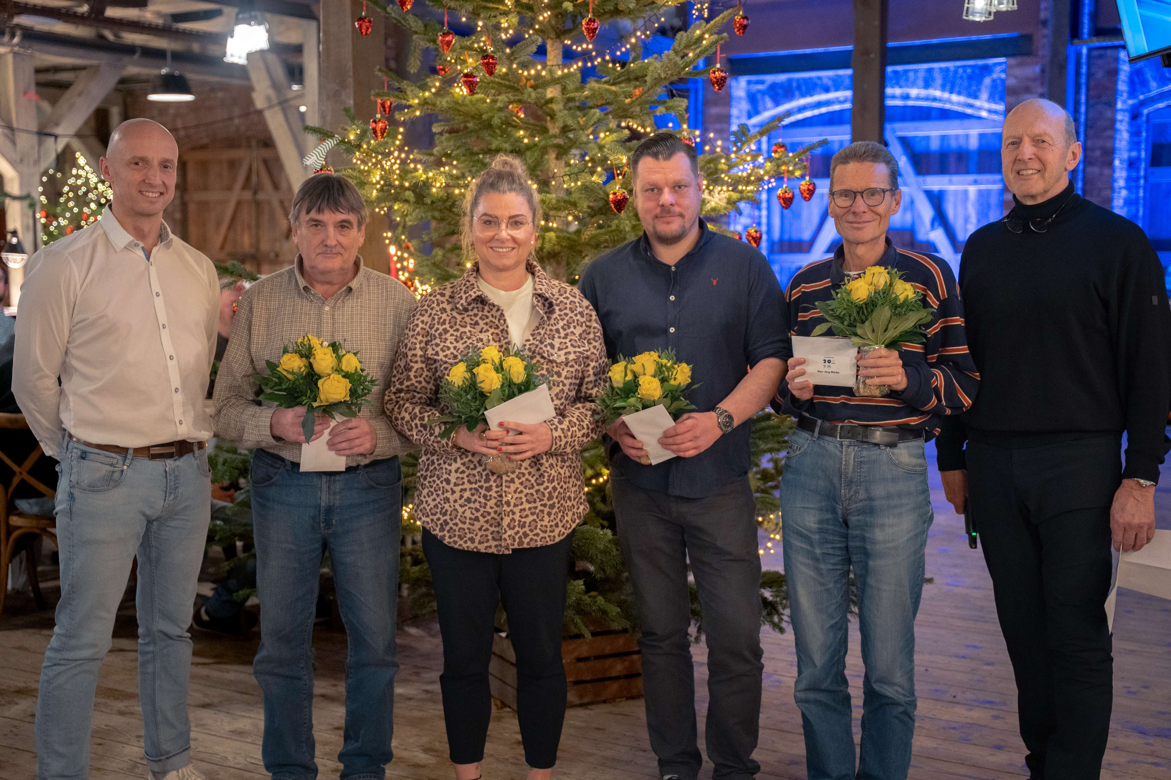 Sechs Personen der Dr. Diestel GmbH stehen vor einem Weihnachtsbaum, zwei mit gelben Blumen.