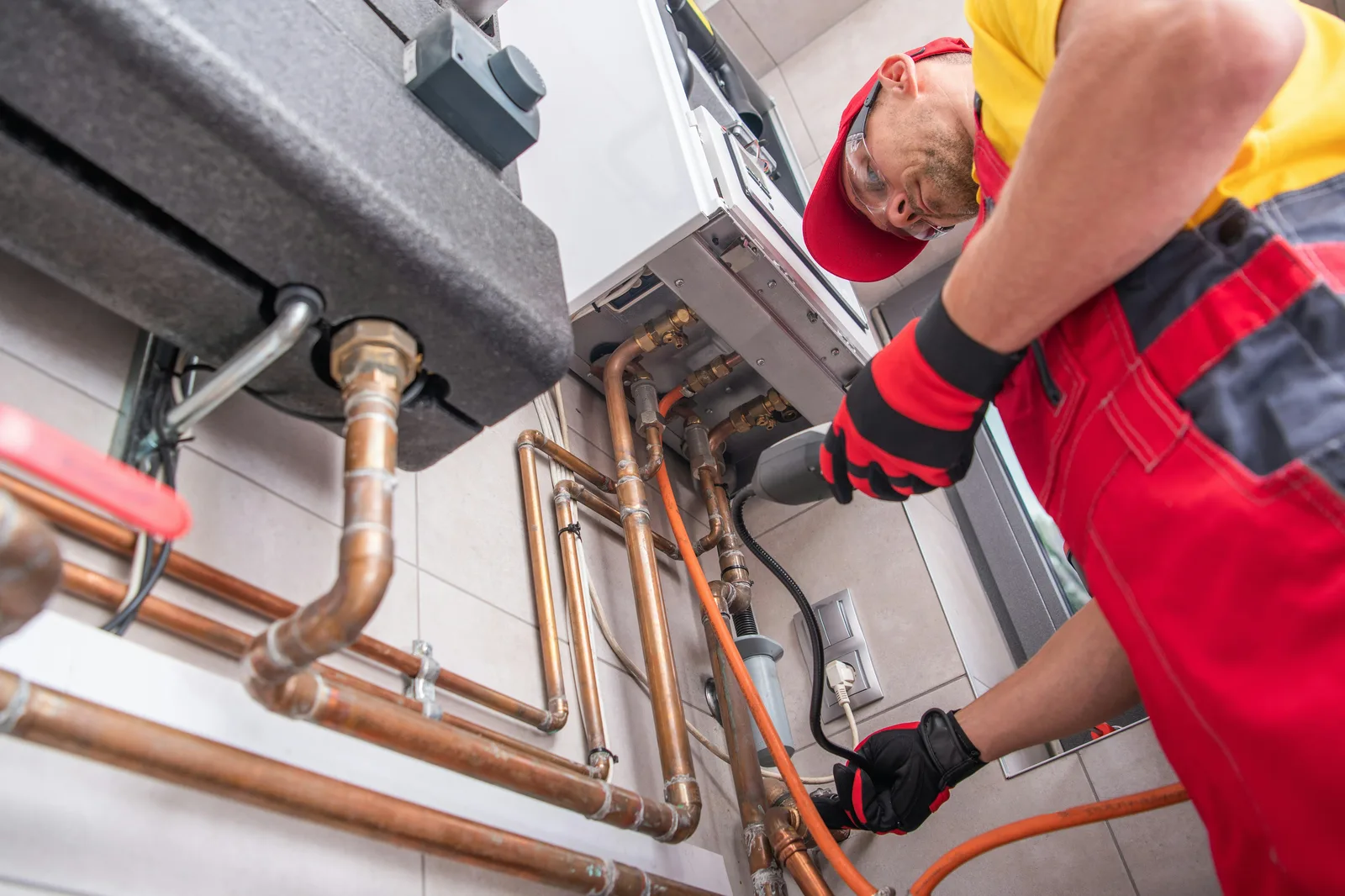 Technician in red overalls servicing copper pipes on gas boiler