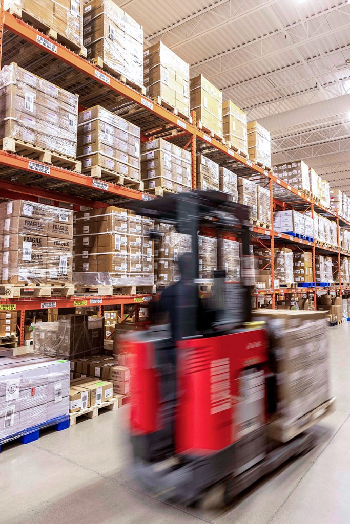A SteriMax warehouse worker pushing a cart of boxed medicines through a warehouse aisle.