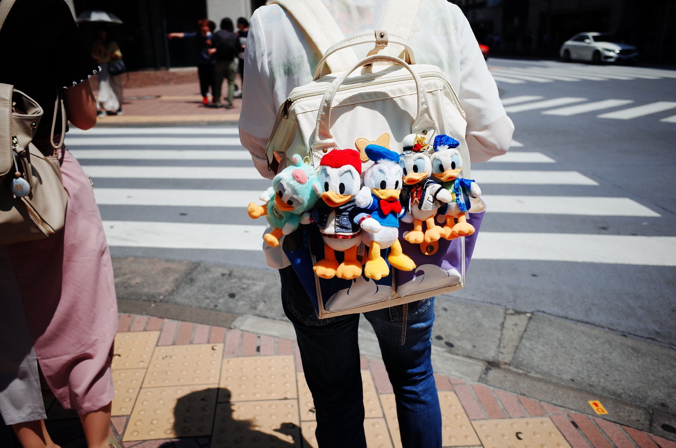 Photographie de rue montrant une femme de dos et son sac à dos qui arbore des peluches de la série Donald Duck