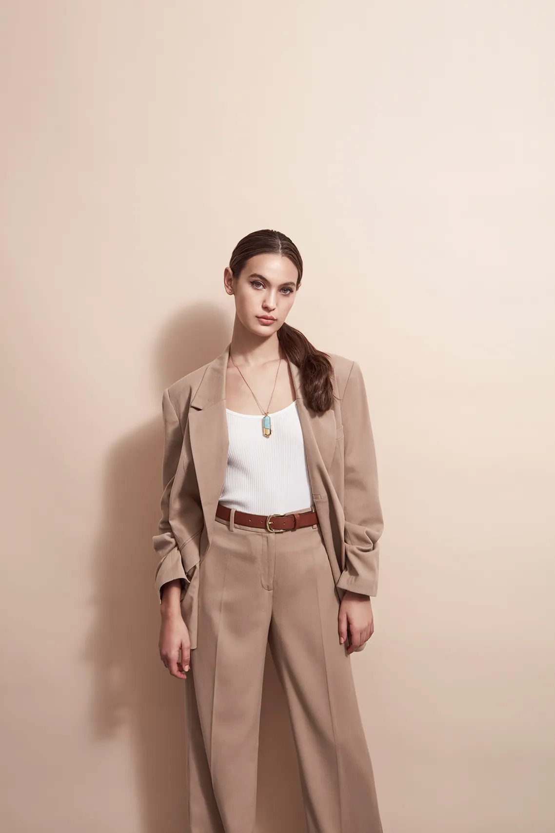 Woman wearing a Talsam smart jewelry charm necklace against a beige background