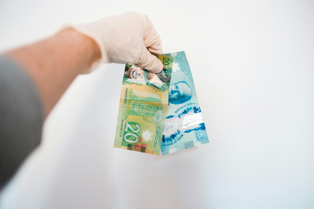 A hand holding physical Canadian twenty and five dollar bills, representing the immediate tax-free cash flow newcomers can unlock by filing Form RC151 themselves, rather than paying an accountant to claim the mythical 'Welcome to Canada' benefit.