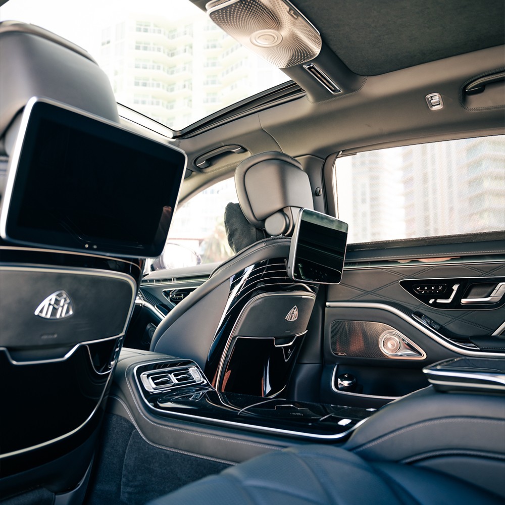 Rear passenger view inside Mercedes-Maybach S580, with individual screens, expansive legroom, and premium amenities.