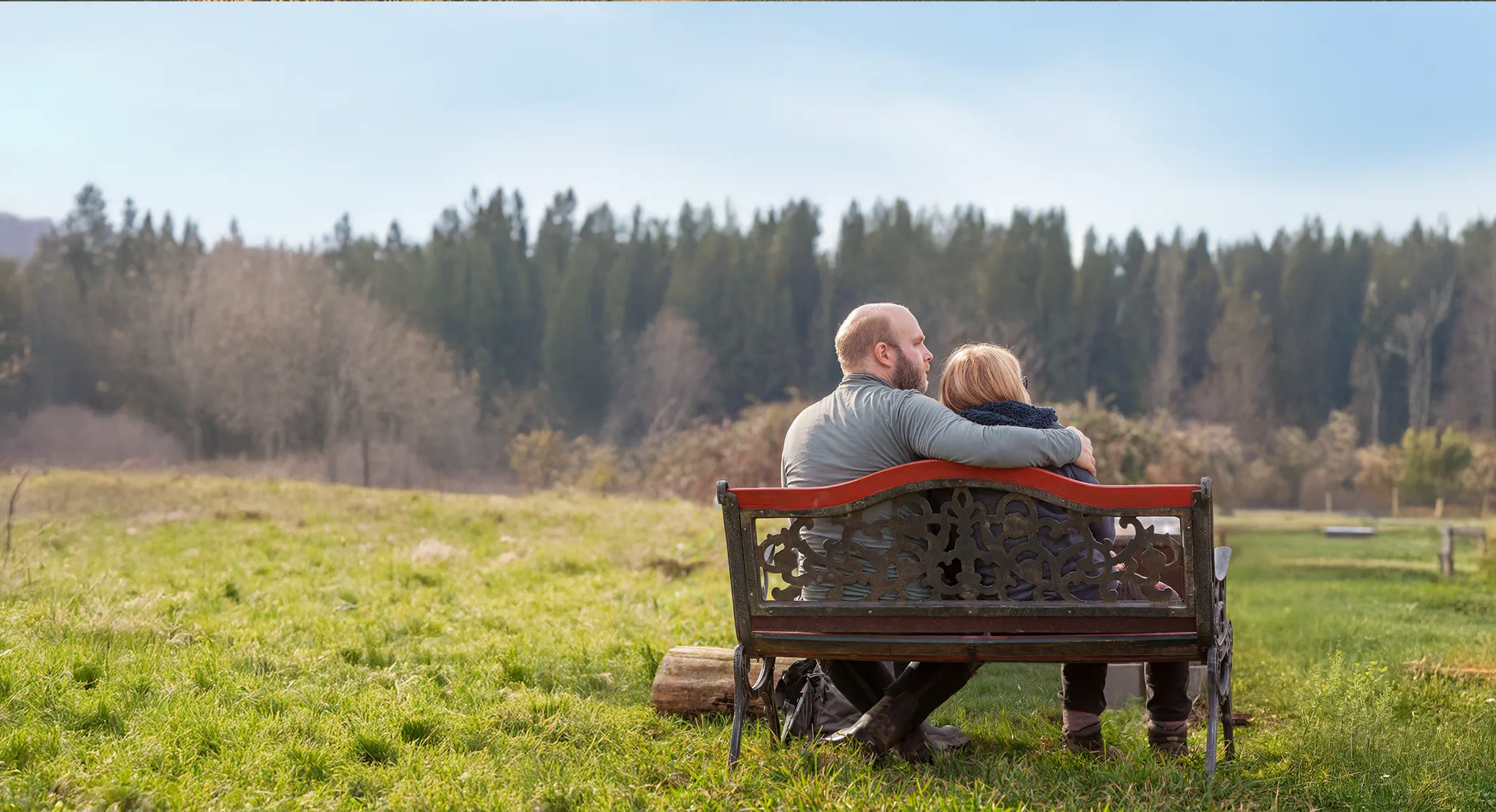 Two people sitting together on a bench overlooking open land and trees at Rooted Northwest.