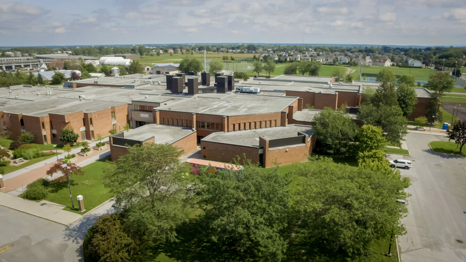 Vue aérienne d’un complexe de bâtiments en brique entouré d’espaces verts et de stationnements.