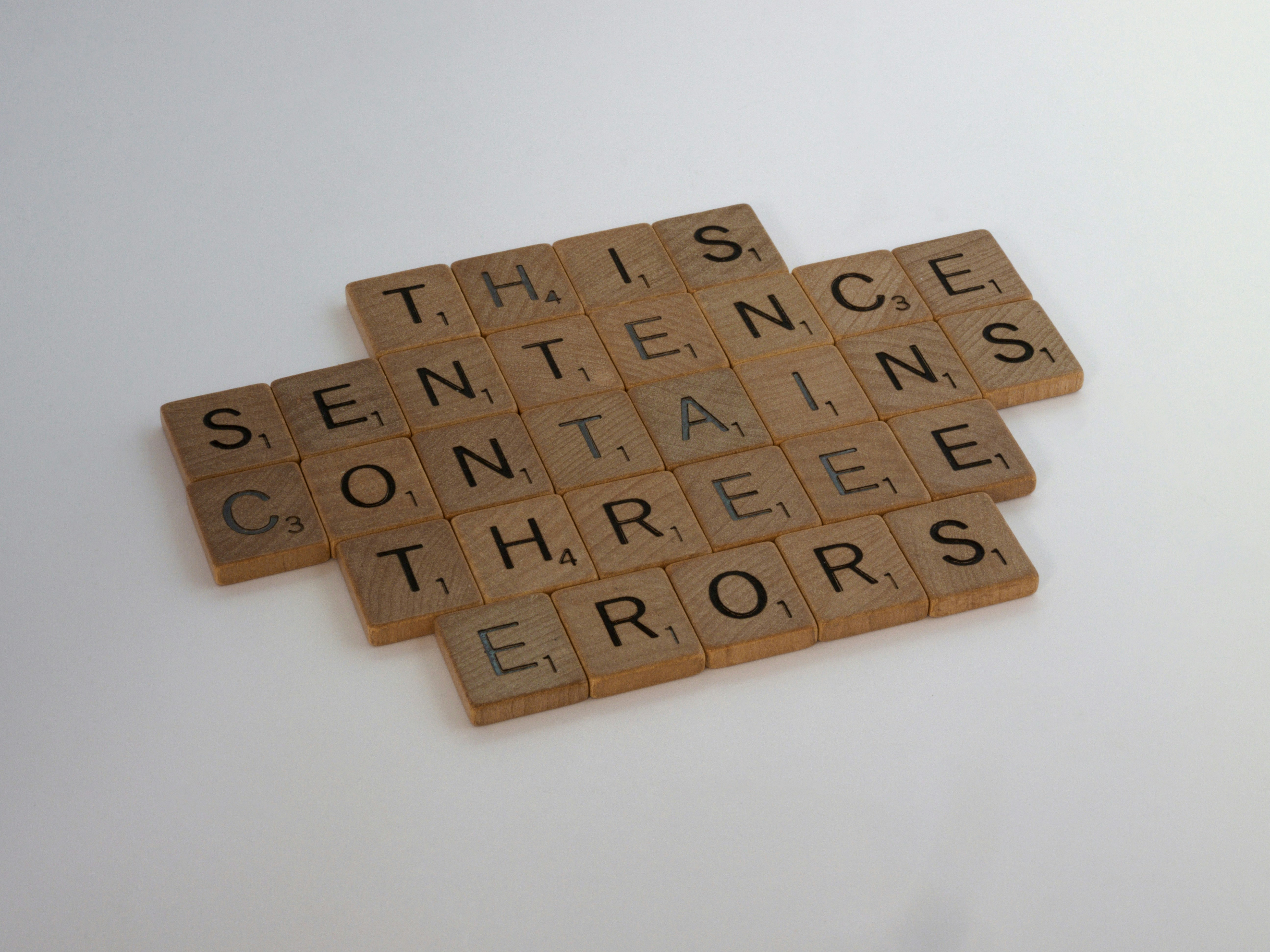 Wooden letter tiles arranged to spell “This sentence contains three errors” on a white background, symbolizing English grammar rules and mistakes.
