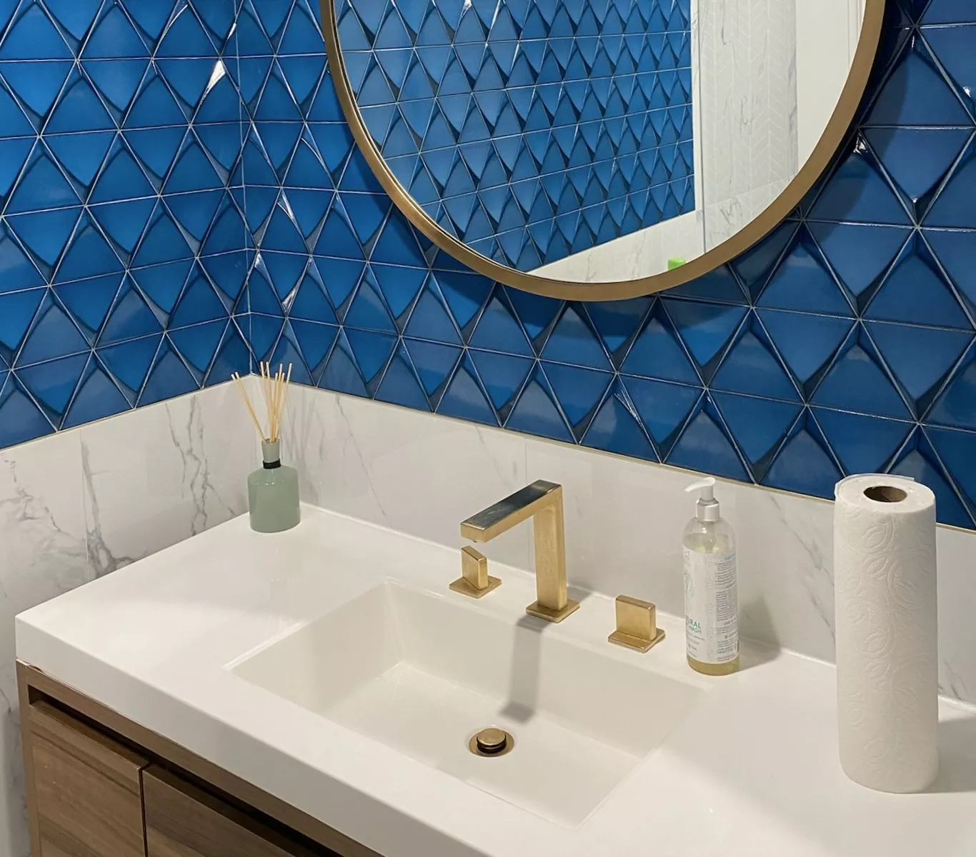 Two men sit at a wooden table with laptops, under a large red lamp. A woman walks by a window. The scene is calm, set against a red-brown wall.