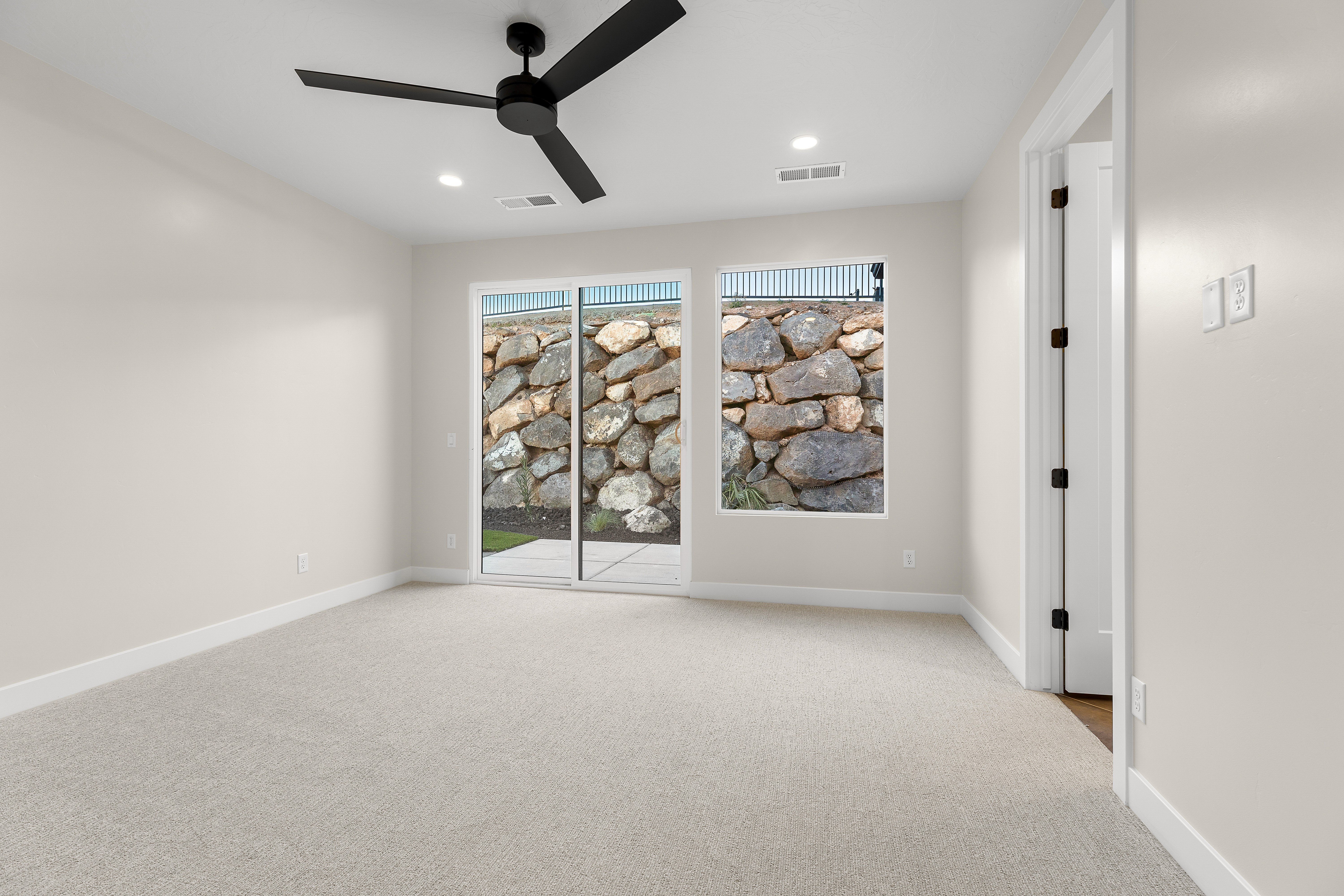 Bedroom with carpeted floor, sliding glass door, and window overlooking the backyard in a Southern Utah home