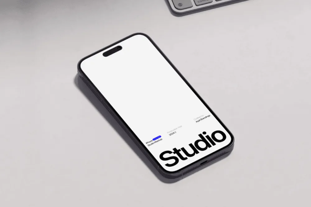 iPhone mockup showcasing a sleek, minimal design on its screen, placed on a smooth, light-colored surface with a partial view of a keyboard in the background. Gentle shadows enhance the composition.