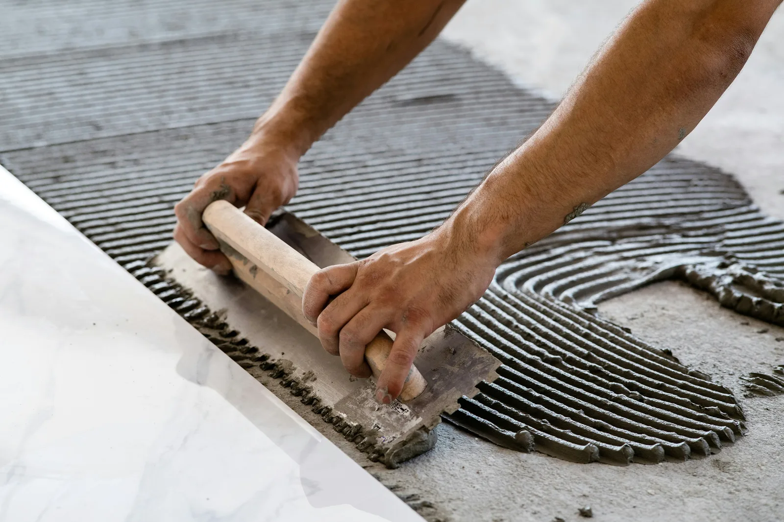 Worker spreading notched adhesive on floor with trowel close-up