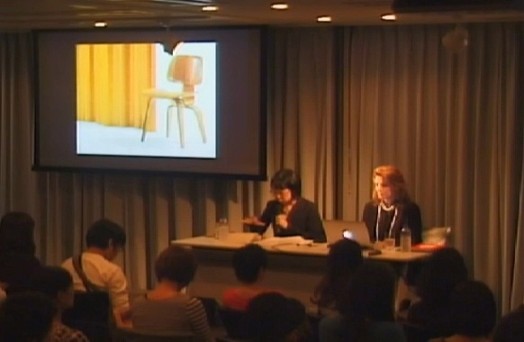 to women giving a presentation from a desk to students, and next to them is an image projected on the wall