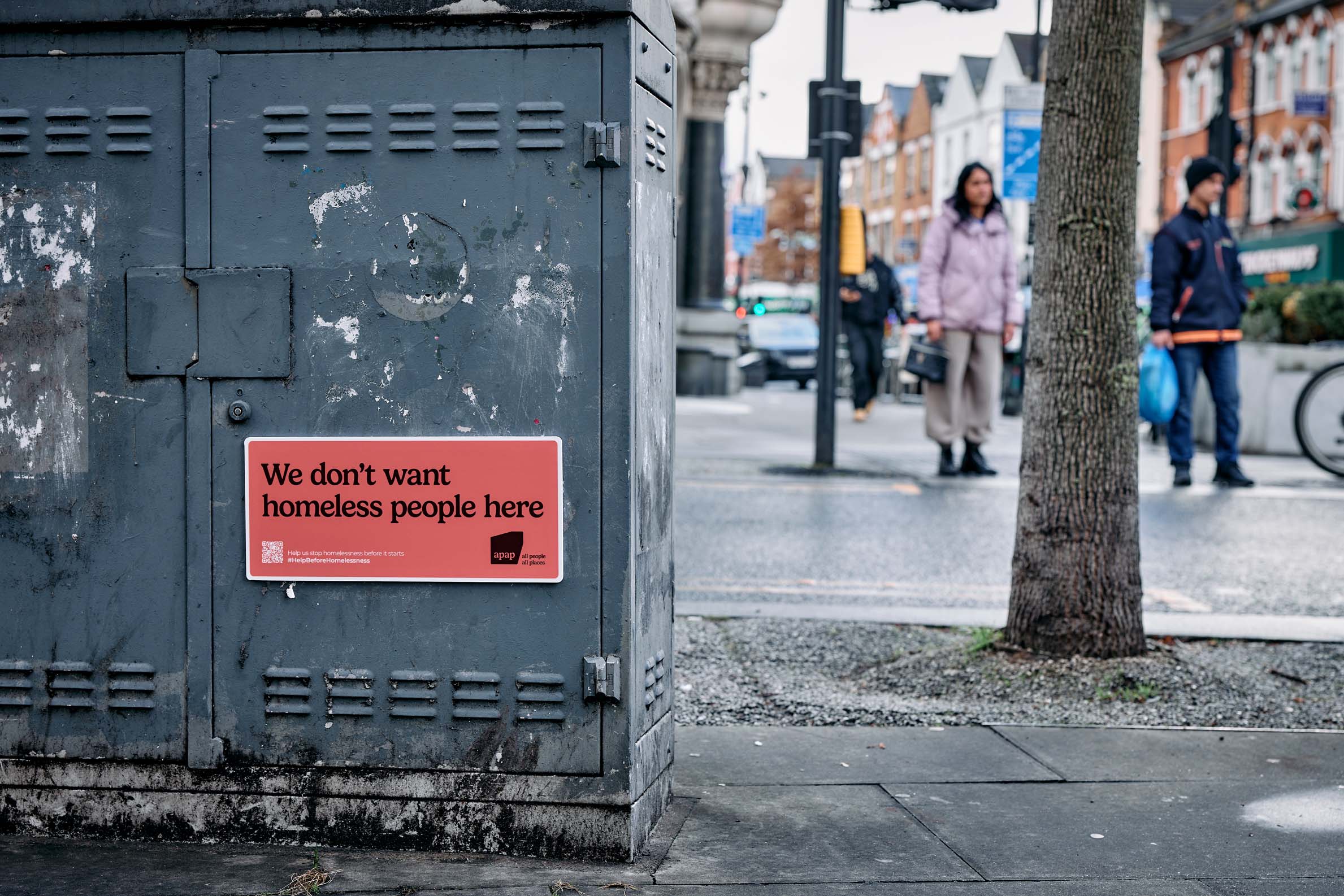 A sign that reads We Don't Want Homeless People here adhered to a cabinet in the street
