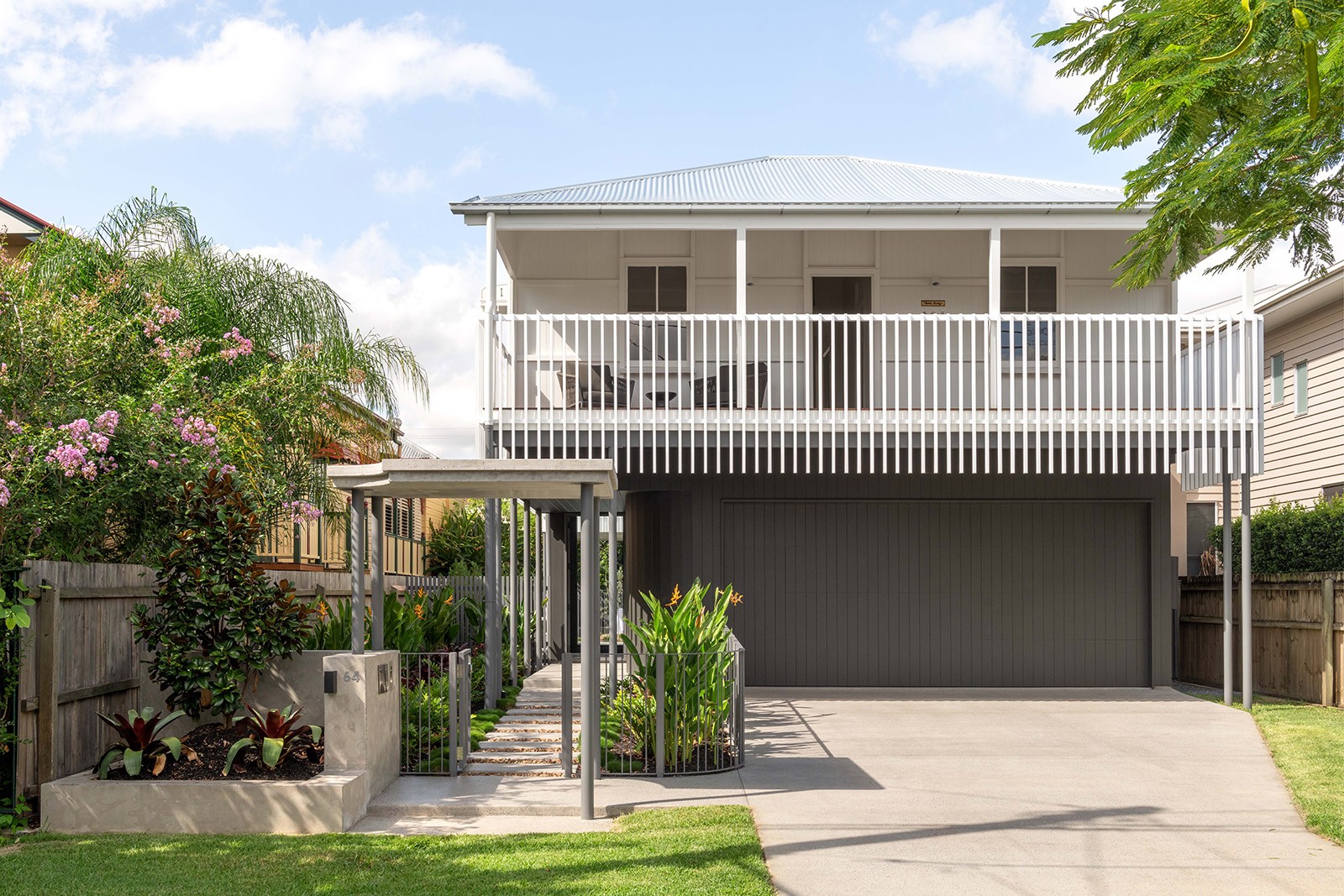 Street-facing view of The Stables, a restored cottage with an elevated verandah and undercroft parking, framed by landscaped gardens and a restrained contemporary addition.