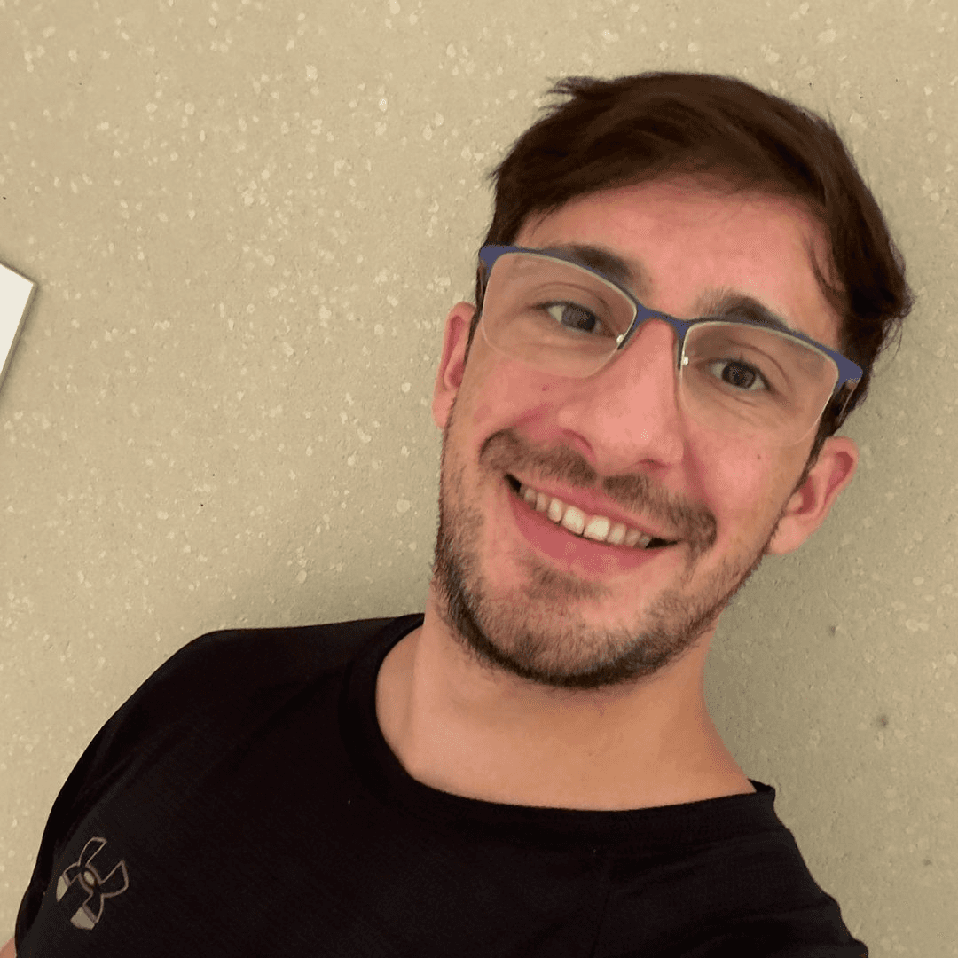 Woman in sunglasses poses against vibrant red background, wearing a beige blazer and black top. Sunlight casts dynamic shadows, creating a stylish, confident mood.