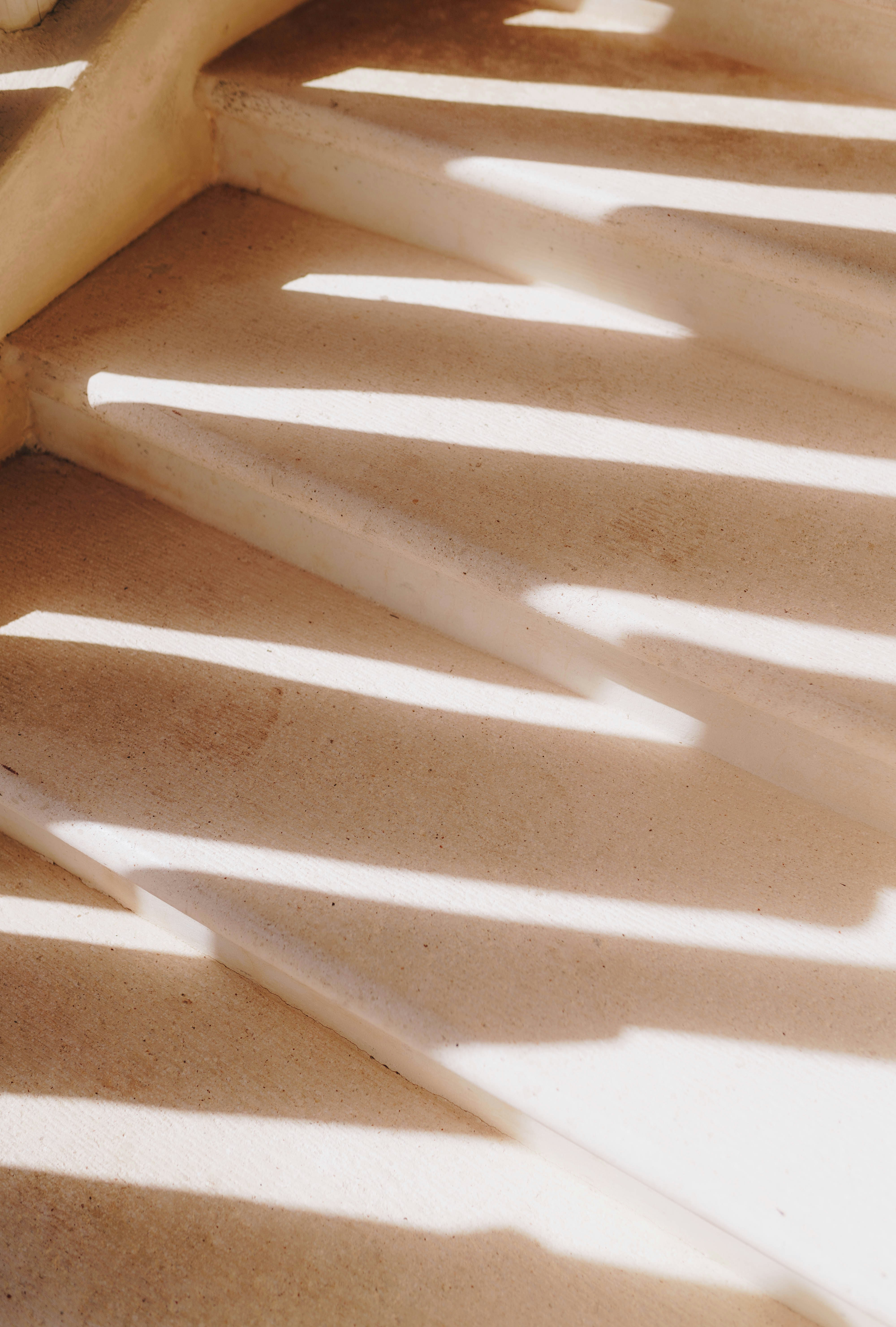 Soft, abstract shadows of light cast across a textured neutral surface, creating a warm, minimal pattern