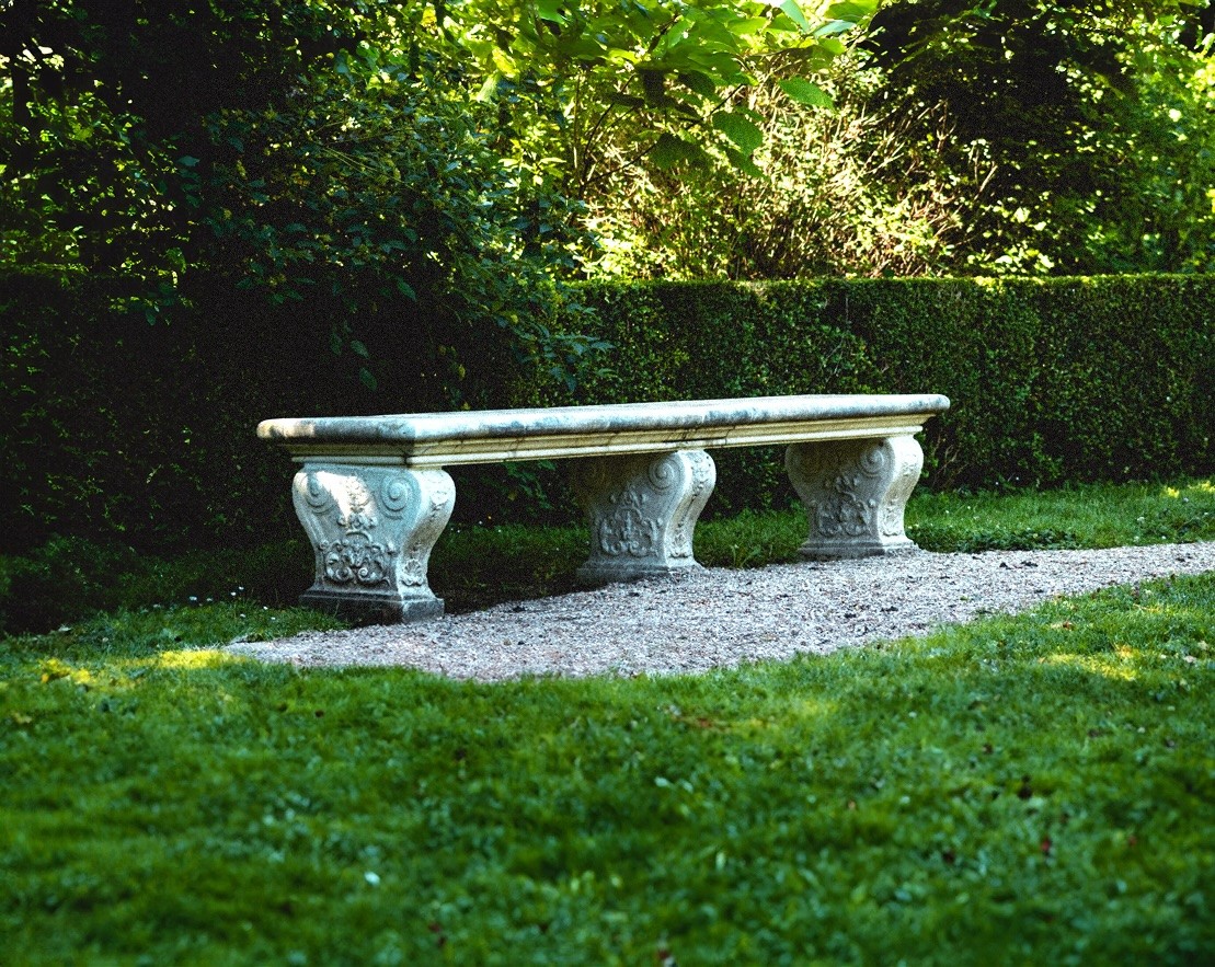 Stone garden bench set within a quiet English garden, representing measured provision and long-term support through trust funds.
