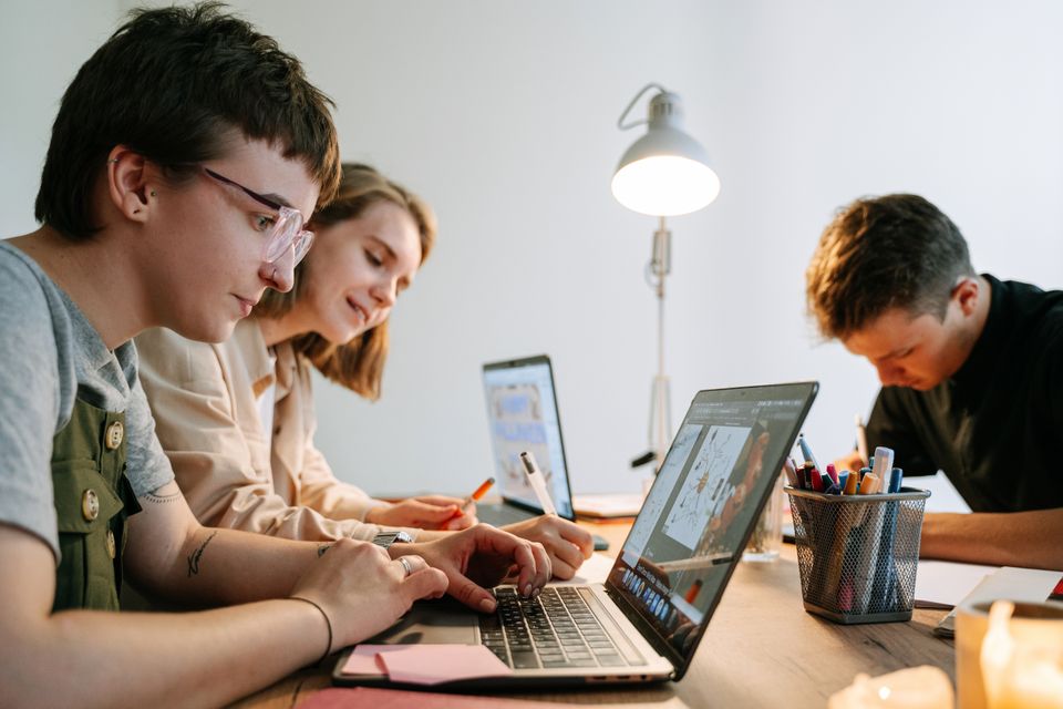 Trois professionnels travaillent ensemble autour d’ordinateurs et de documents dans un atelier créatif.