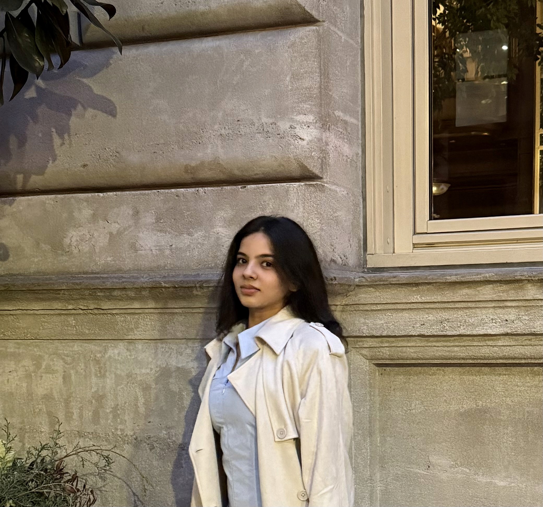 Minimal studio portrait of a confident woman in a white shirt, arms crossed, on a soft gray background.