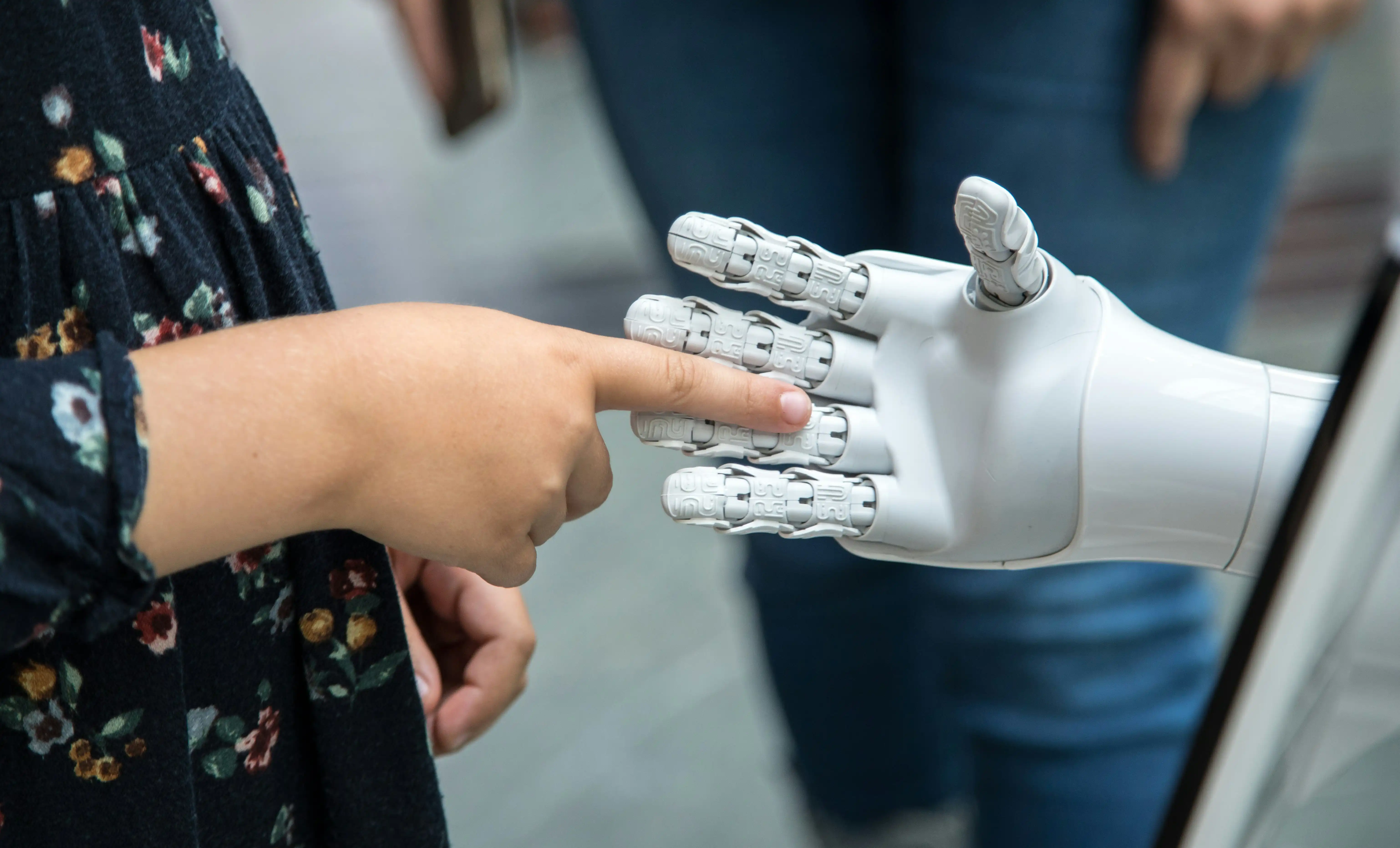 Human hand touching the fingers of a white robotic hand