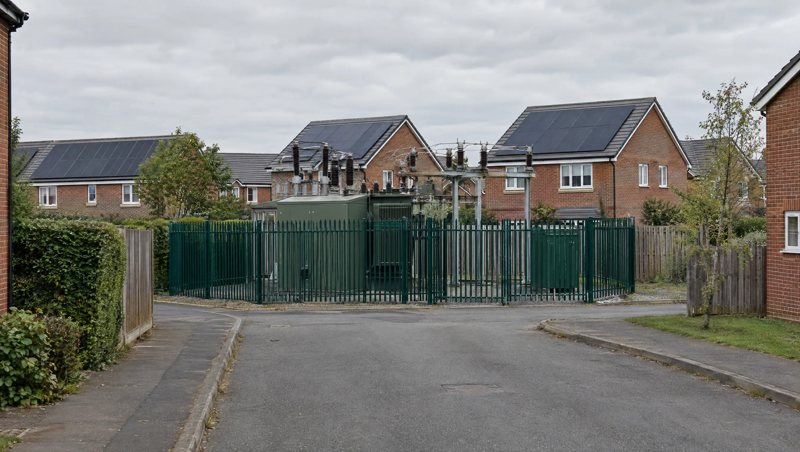 An electricity substation at the end of a residential street with solar panels on nearby roofs