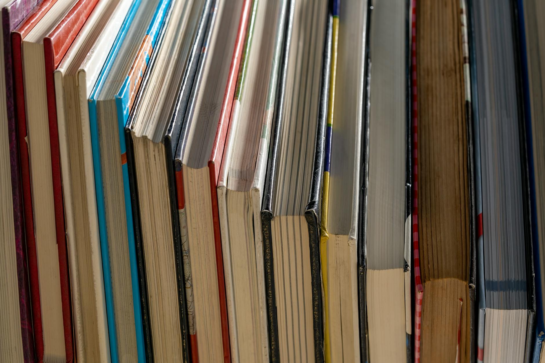 A stack of various hardcover children's books resting on a teacher's desk next to a potted plant and a coffee mug.