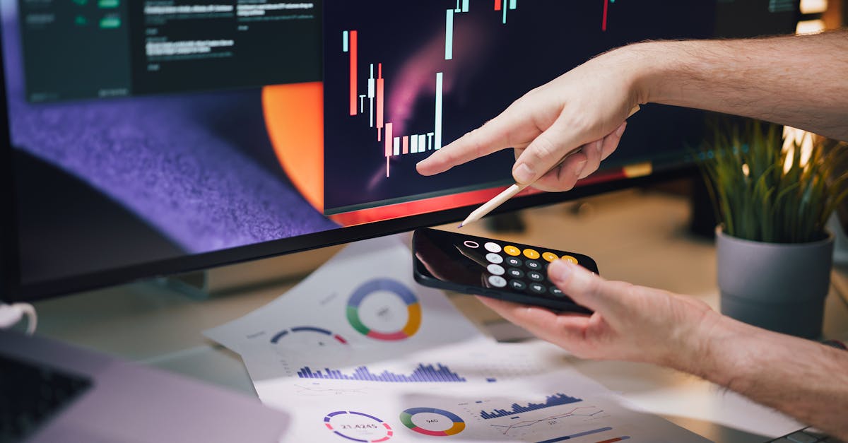 Hands analyzing stock market data on monitor and smartphone in office setting.