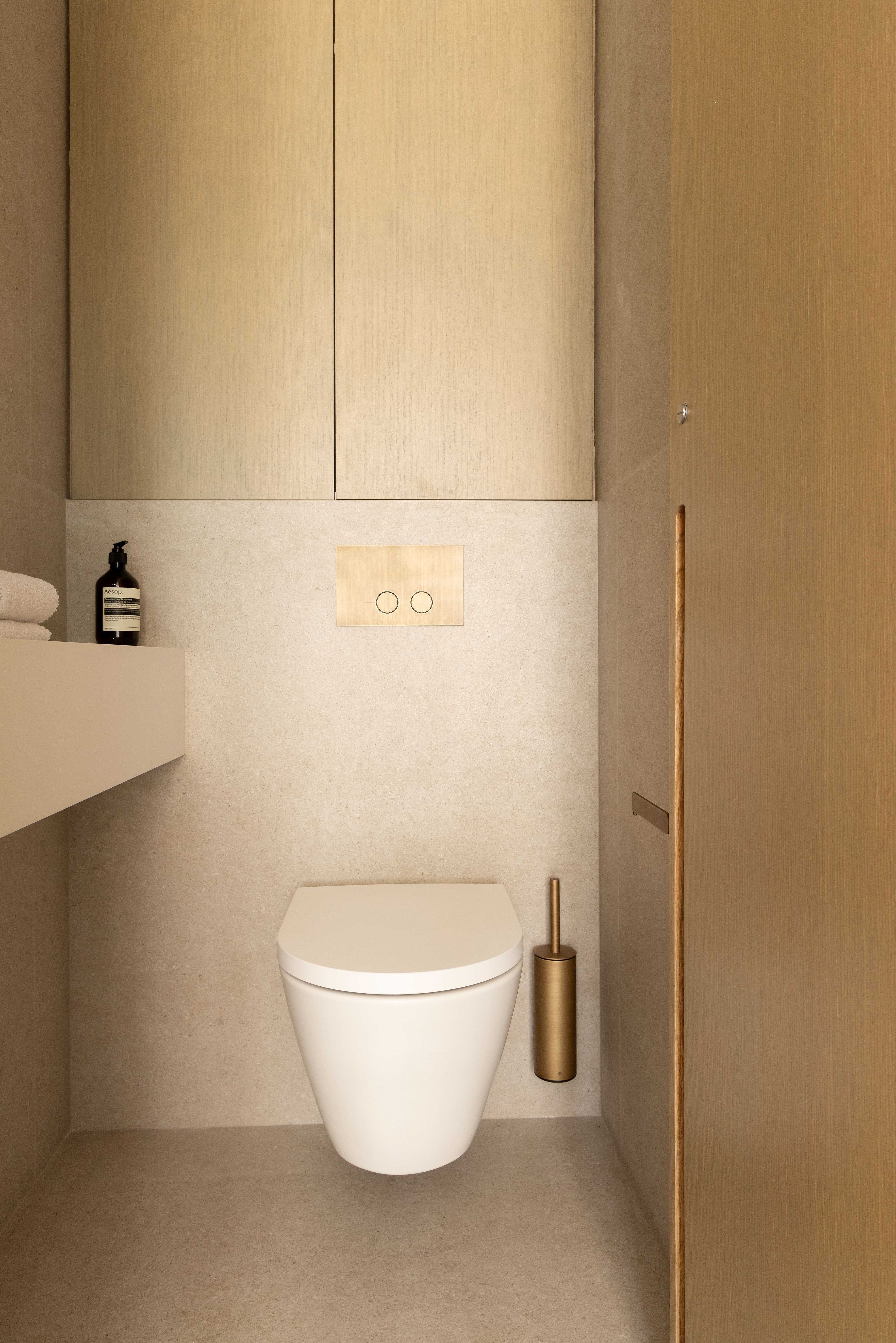 Toilettes suspendues avec placard en bois clair, bouton-poussoir doré et balai
