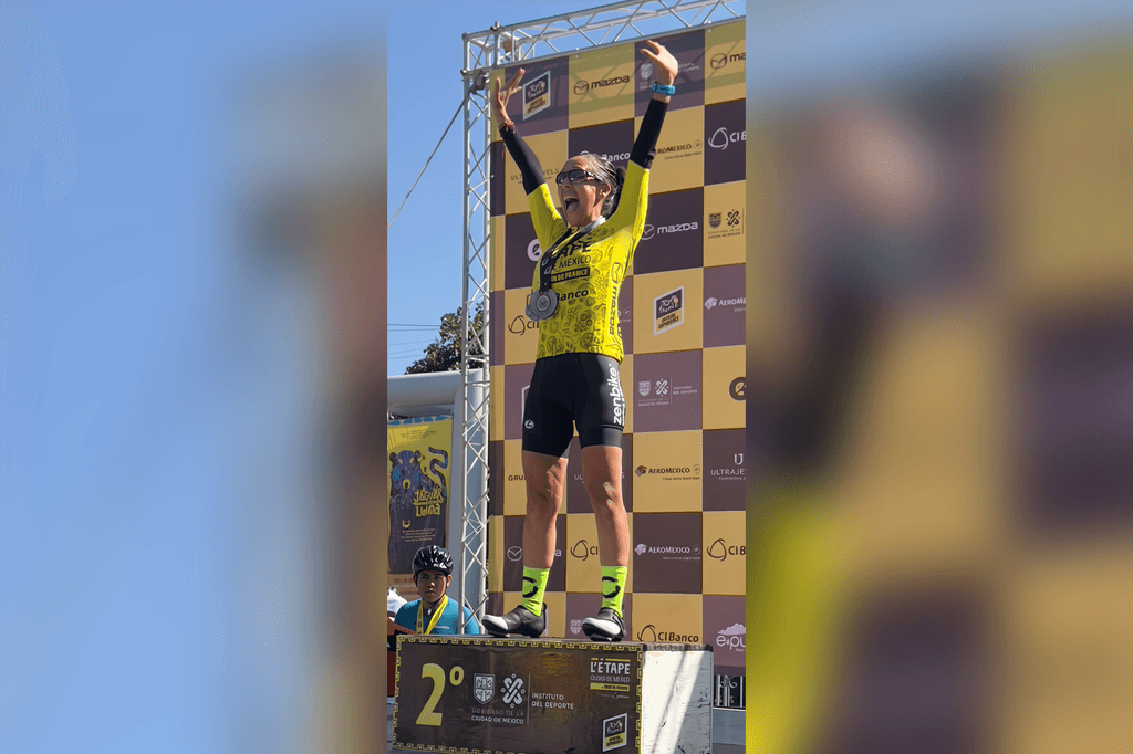 Ciclista en el podio celebrando su segundo lugar con los brazos en alto y uniforme del equipo.