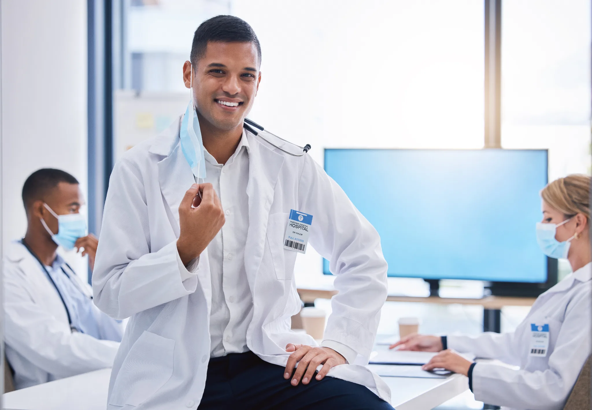 Smiling male physician in white coat removing his face mask.