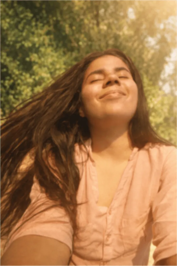 A young woman with long hair smiles in a natural setting.