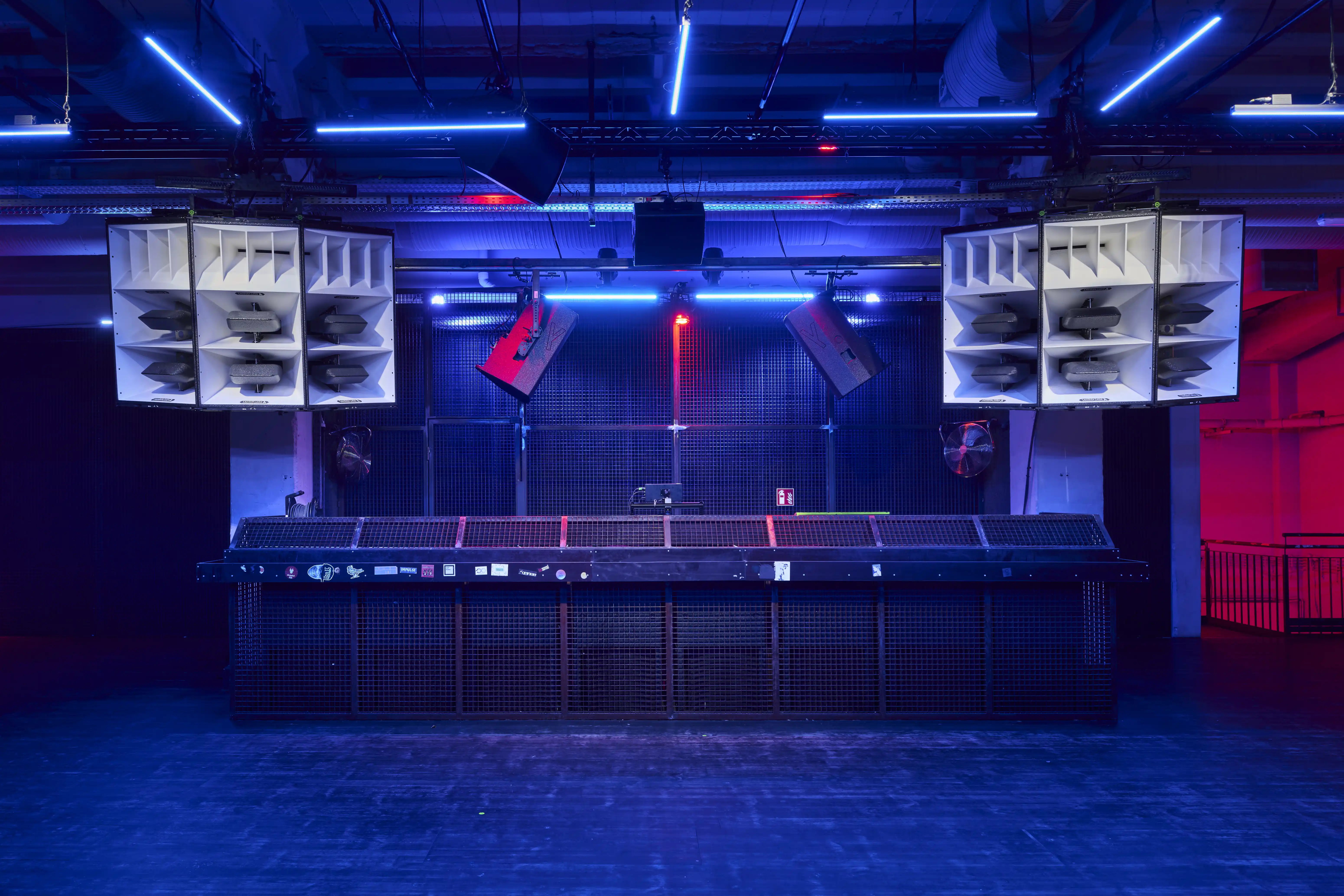 DJ stage at TRESOR GLOBUS framed by two large white horn speaker clusters, a long mesh-fronted booth and blue neon tubes across the industrial ceiling.