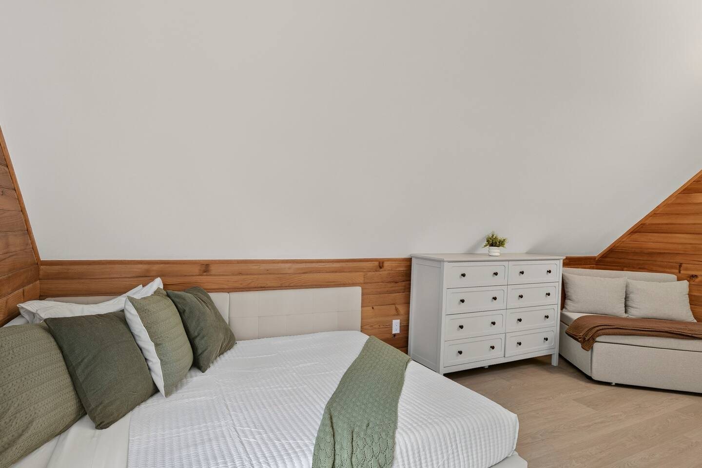 Bed under a sloping ceiling with a white dresser and a sleeper chair