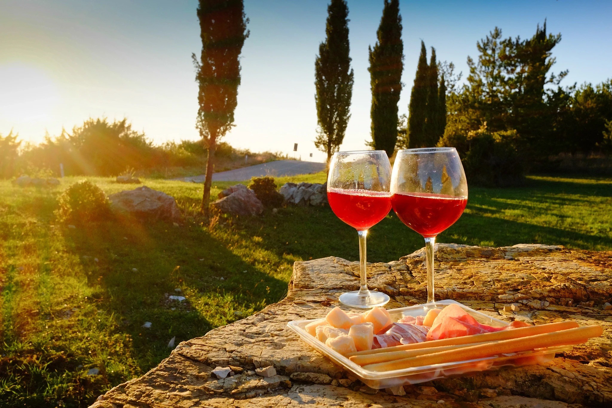 Two wine glasses and a plate of cheese and crackers in a bright outdoors vineyard location