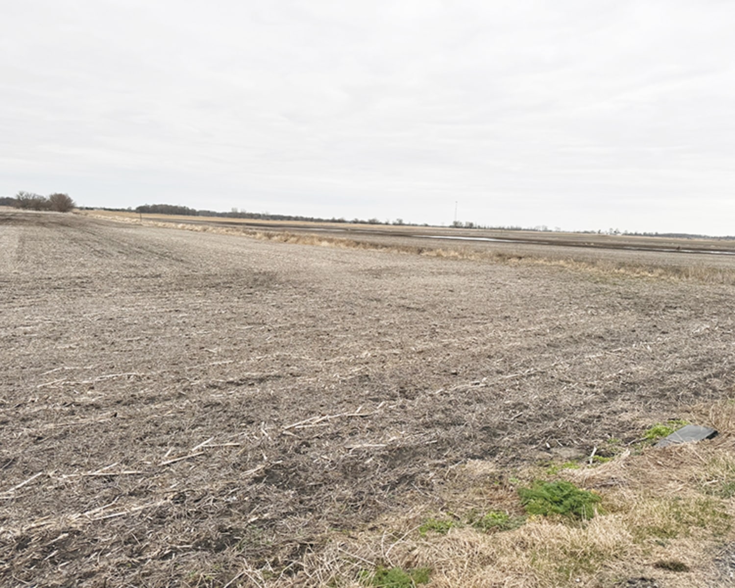 Barren farmland stretching to the horizon under a cloudy sky, with dry soil and sparse vegetation.