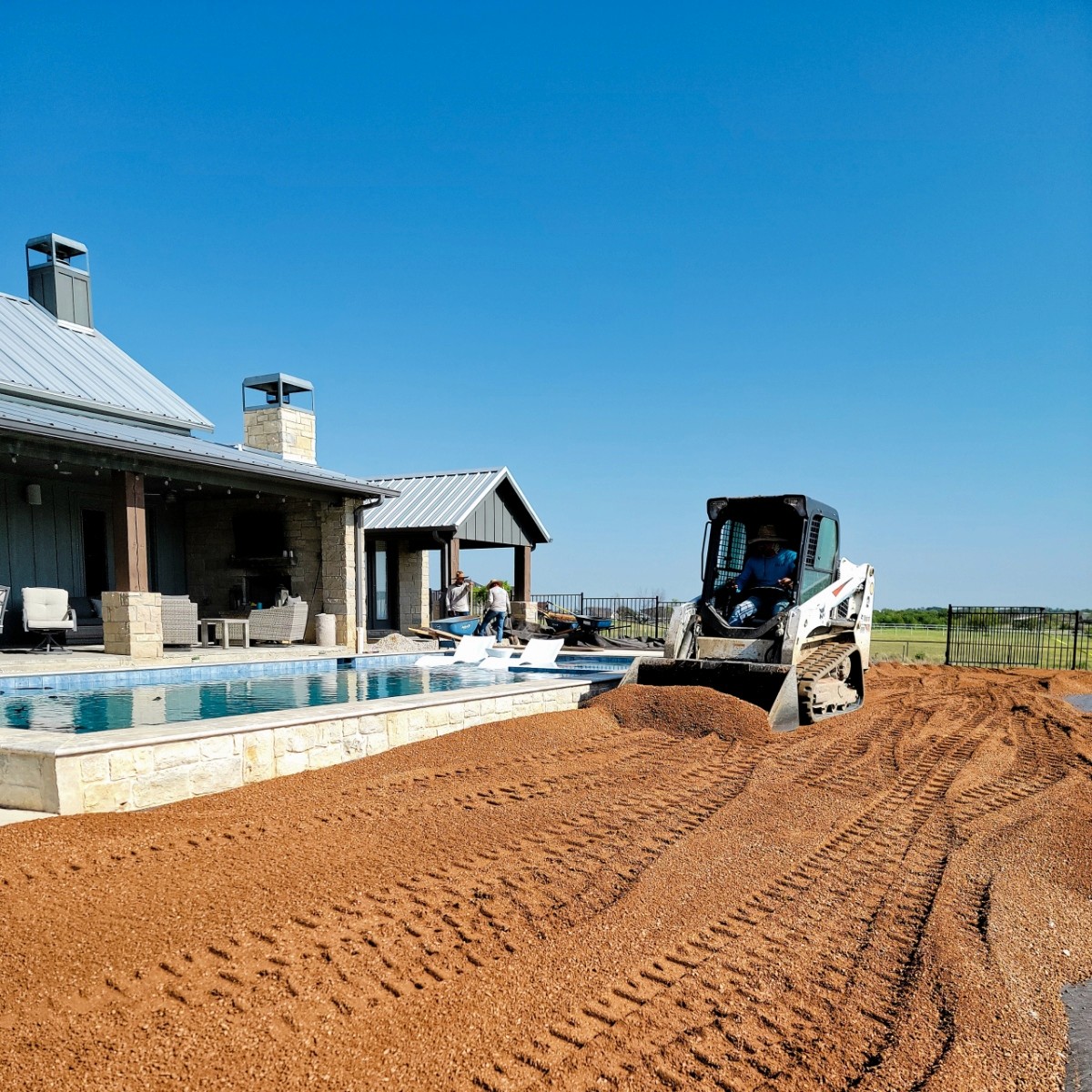 Elite Landscaping DFW crew member operates a skid steer to meticulously grade the aggregate sub-base for an artificial turf installation next to a modern pool in Fort Worth, Texas
