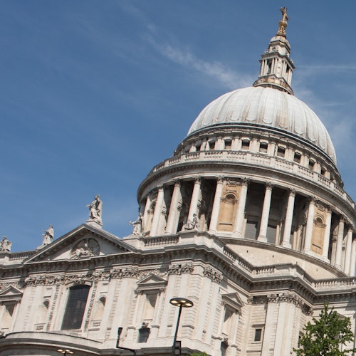 Een groot, historisch gebouw met een koepel, zuilen en verfijnde stenen details onder een helderblauwe lucht.
