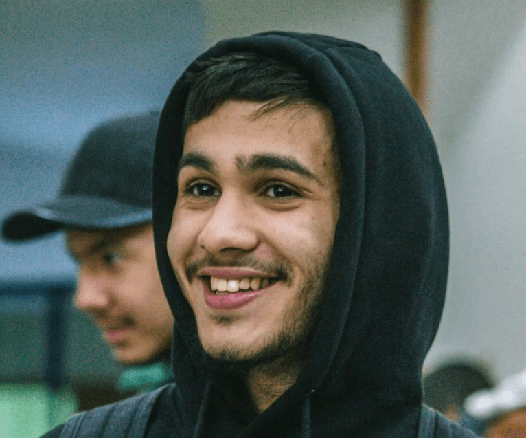 a young man wearing glasses standing in front of a mountain