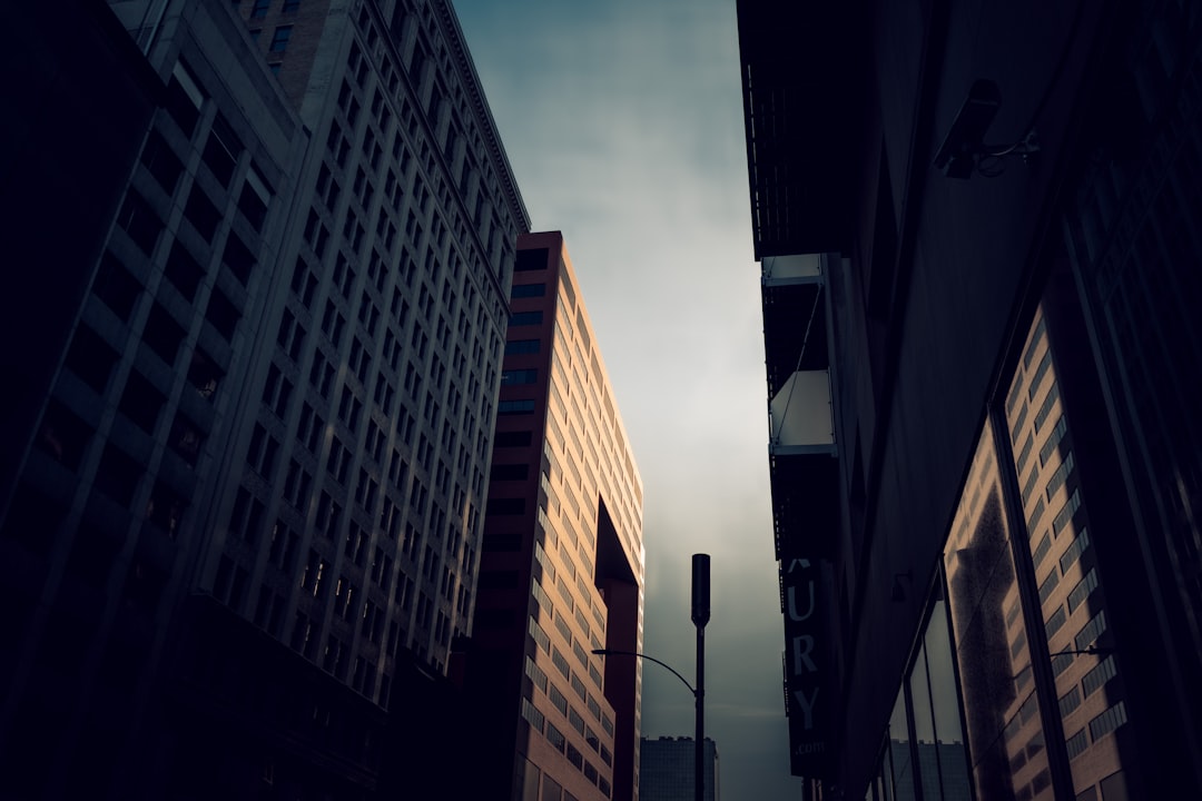 Low-angle street view looking up between tall dark office buildings toward a narrow sky.