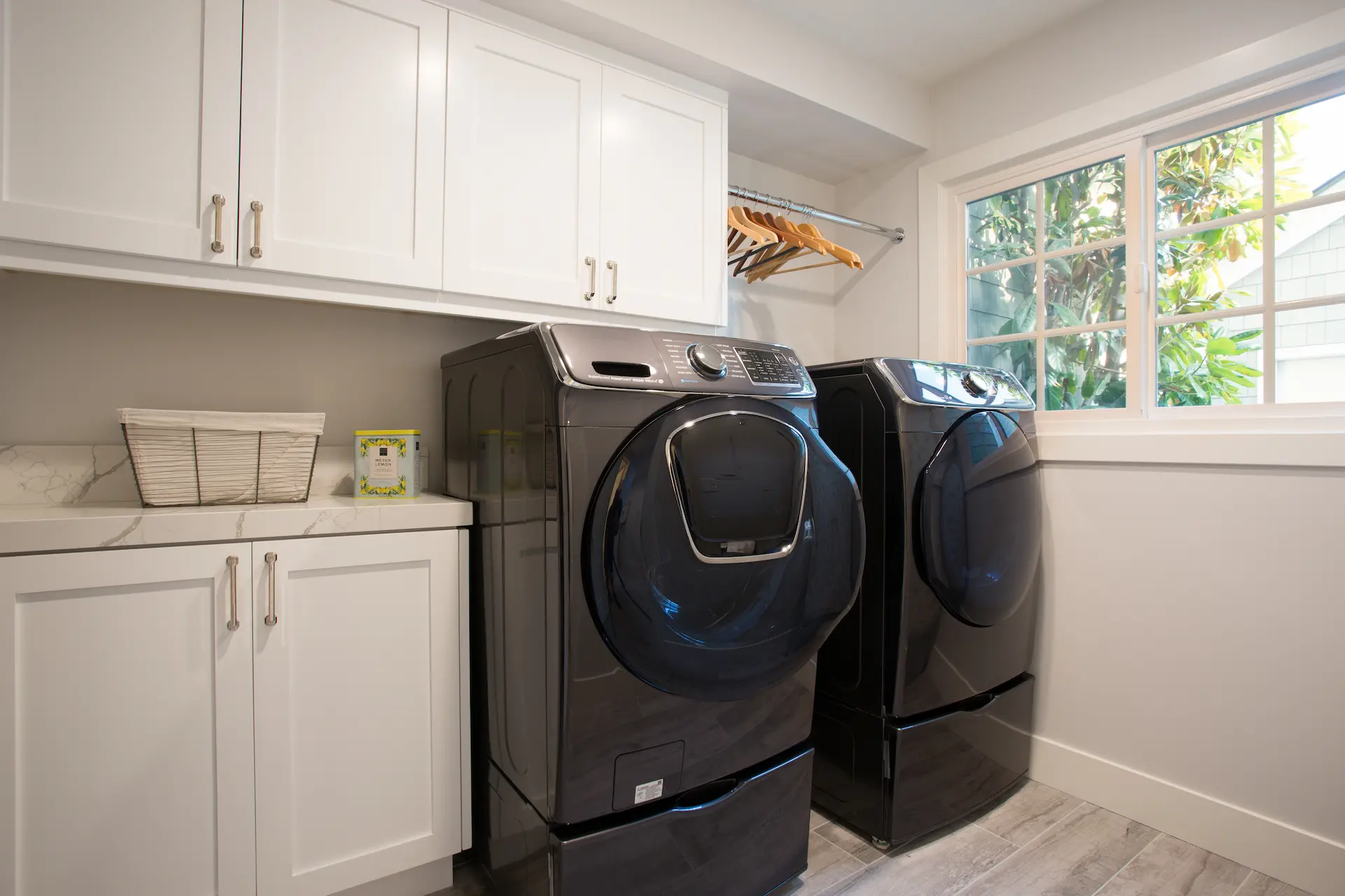 Laundry room with dark grey appliances and white cabinets. Sliding window with white trim. From Dana Point Cape Cod remodel, photo by Chris Darnall.