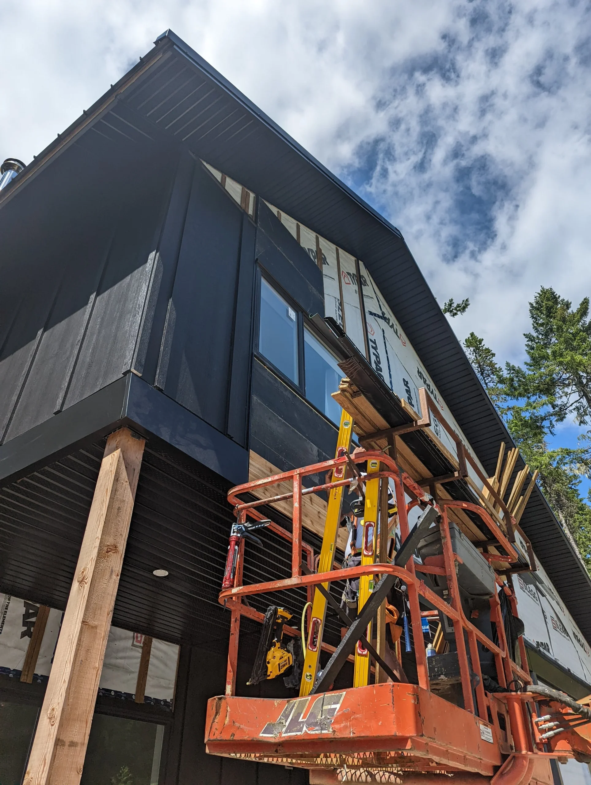 Modern two-story home with large glass windows, warmly lit interiors, and a balcony. Surrounded by trees and a manicured lawn at dusk. Cozy ambiance.