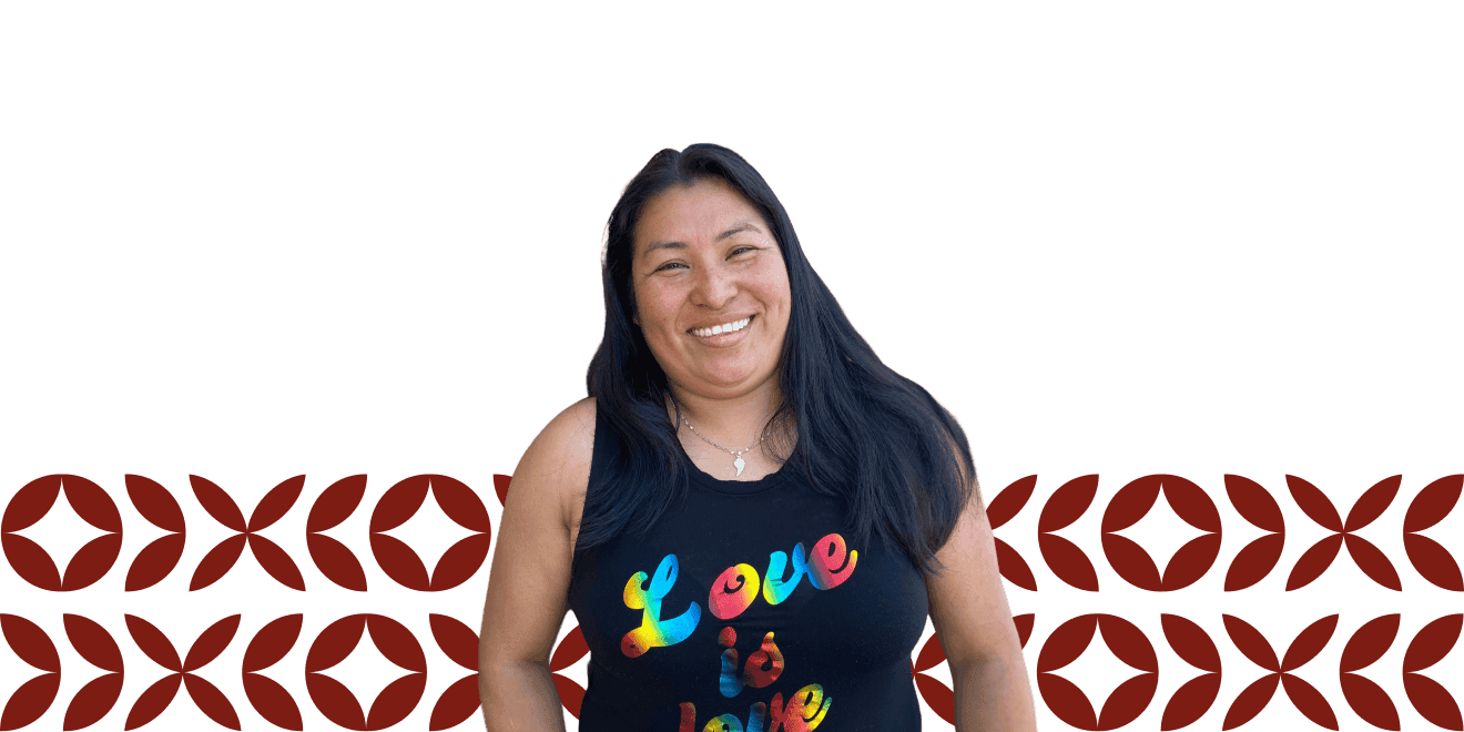 Uma mulher com cabelo longo e escuro sorri enquanto veste uma regata preta com a mensagem colorida "Love is Love", posicionada contra um fundo transparente com um padrão decorativo vermelho ao longo da parte inferior.